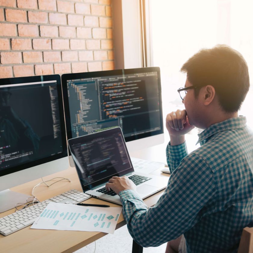 A person sits at their desk in front of multiple screens while concentrating on a task.