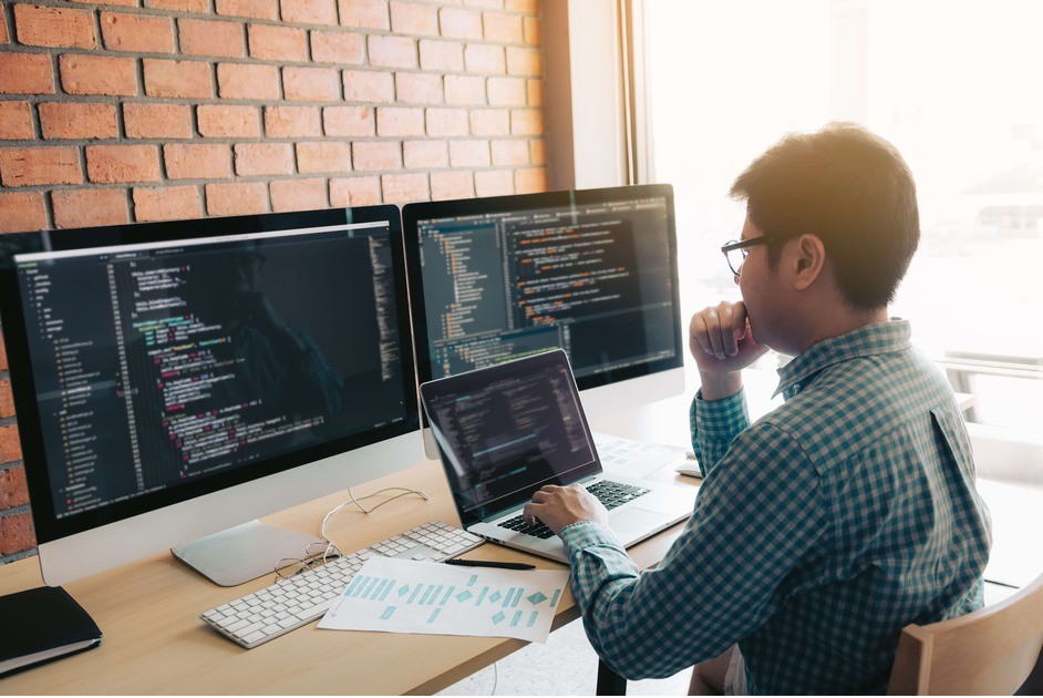 A person sits at their desk in front of multiple screens while concentrating on a task.