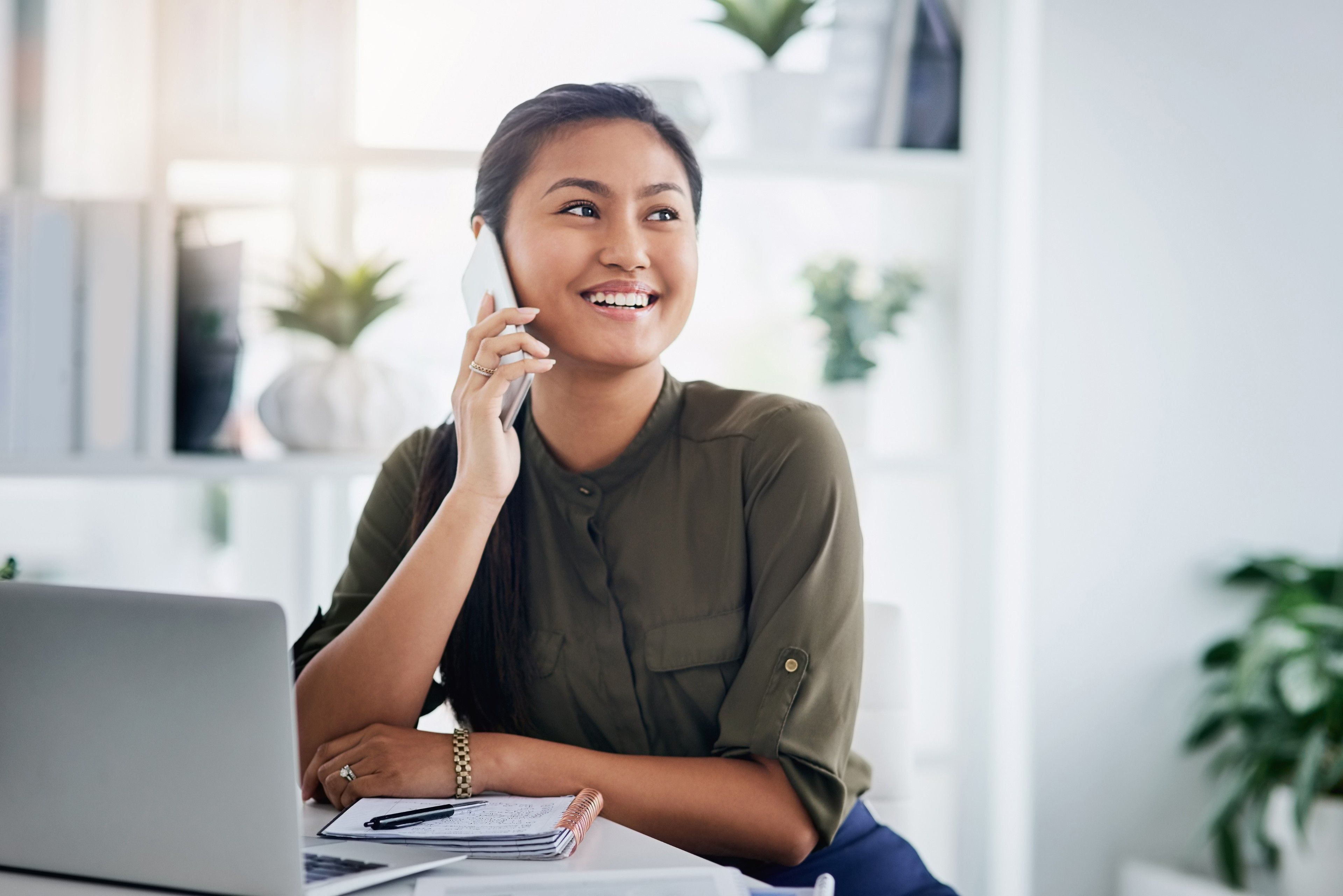 A person talks on the phone while sitting with their laptop and smiling.