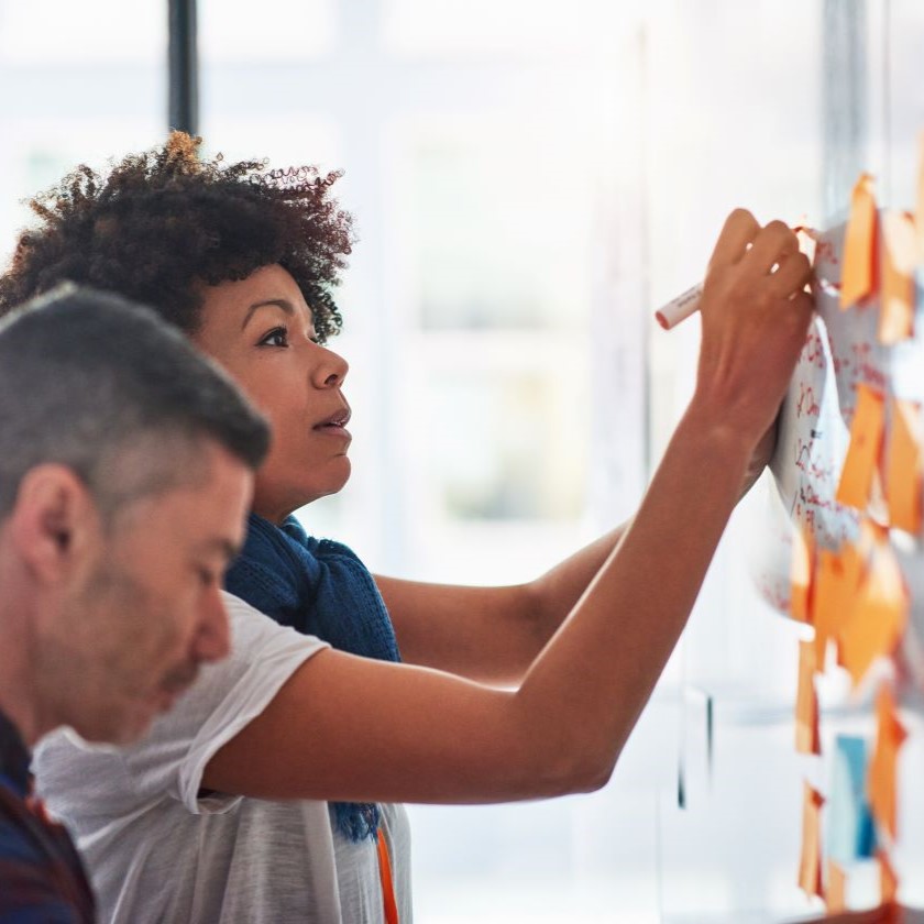 A person writing on a whiteboard surrounded by notes while working on personalized content strategy with another colleague.