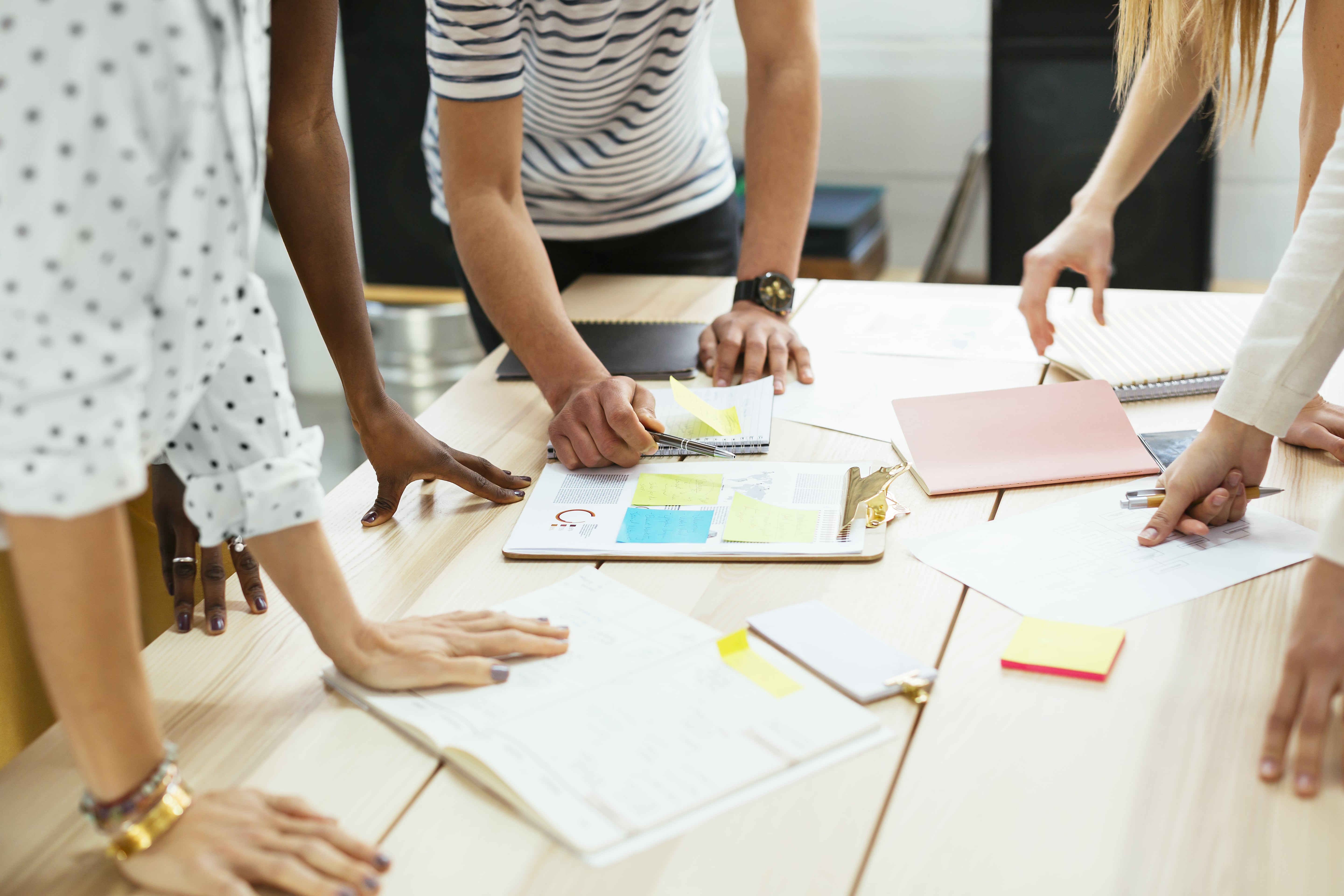 A group of people stand around an office table with scattered notes and papers while planning together.
