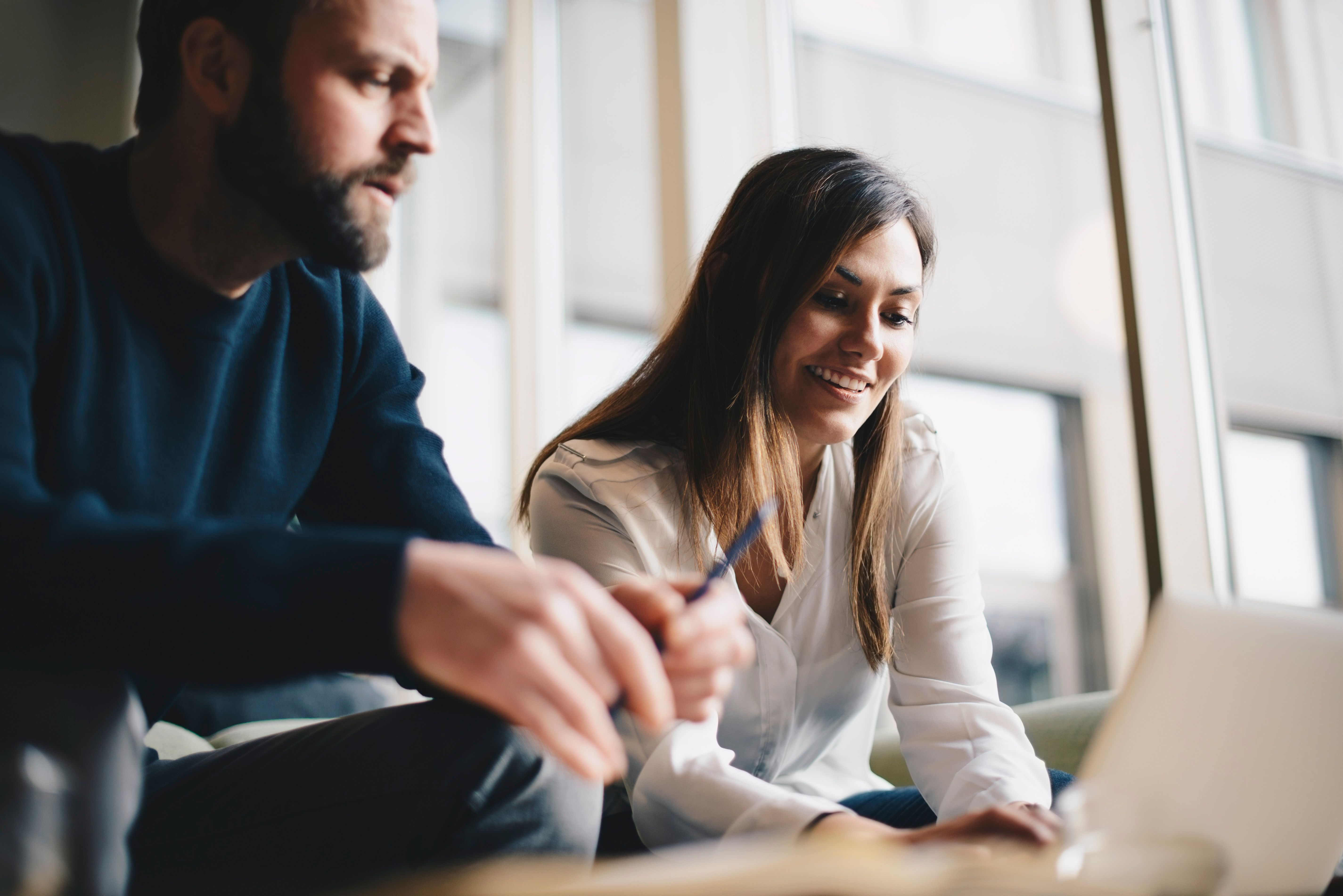 Two people sit at a laptop in a breakout space and smile while repurposing a blog.