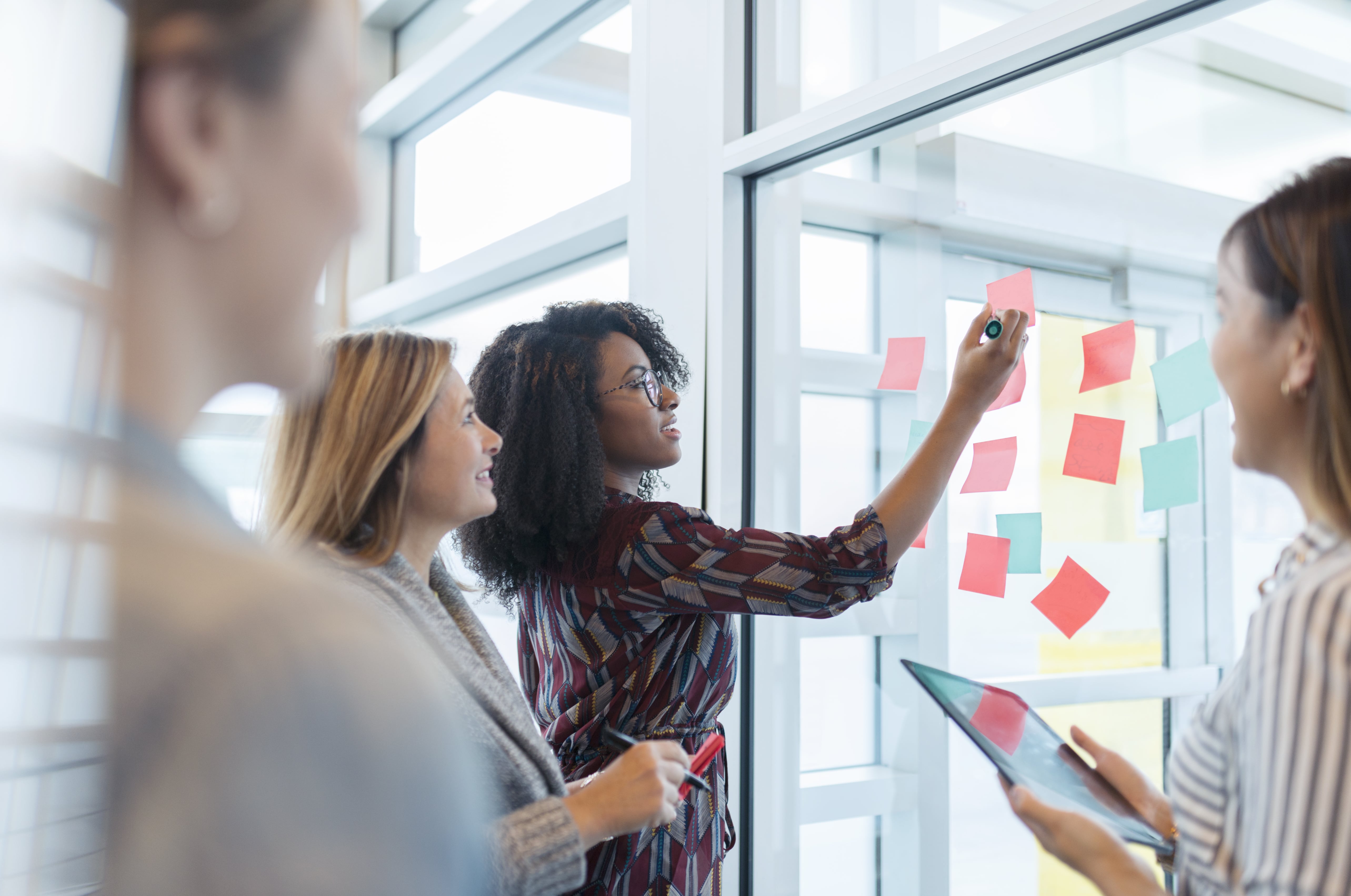 A person writing on a whiteboard covered with sticky notes, collaborating with teammates during an ideation session.