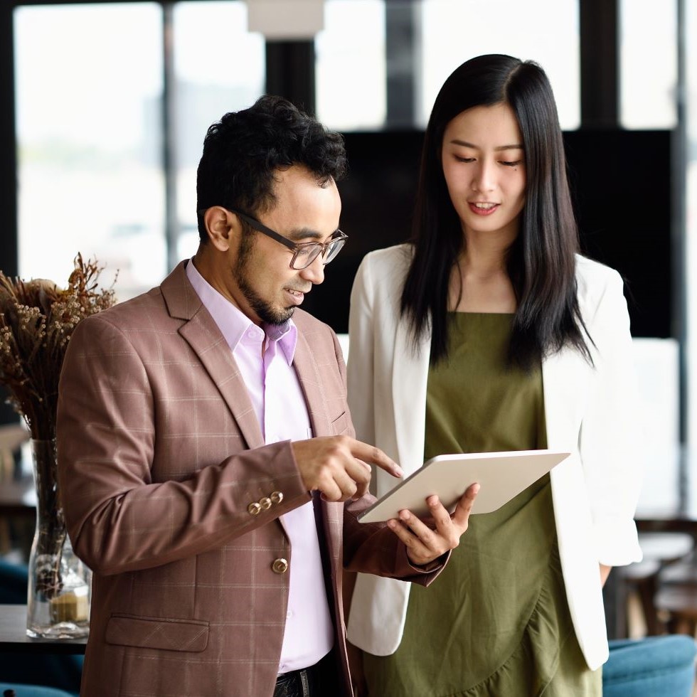 Two coworkers using a tablet to collaborate handoffs in a shared office setting.