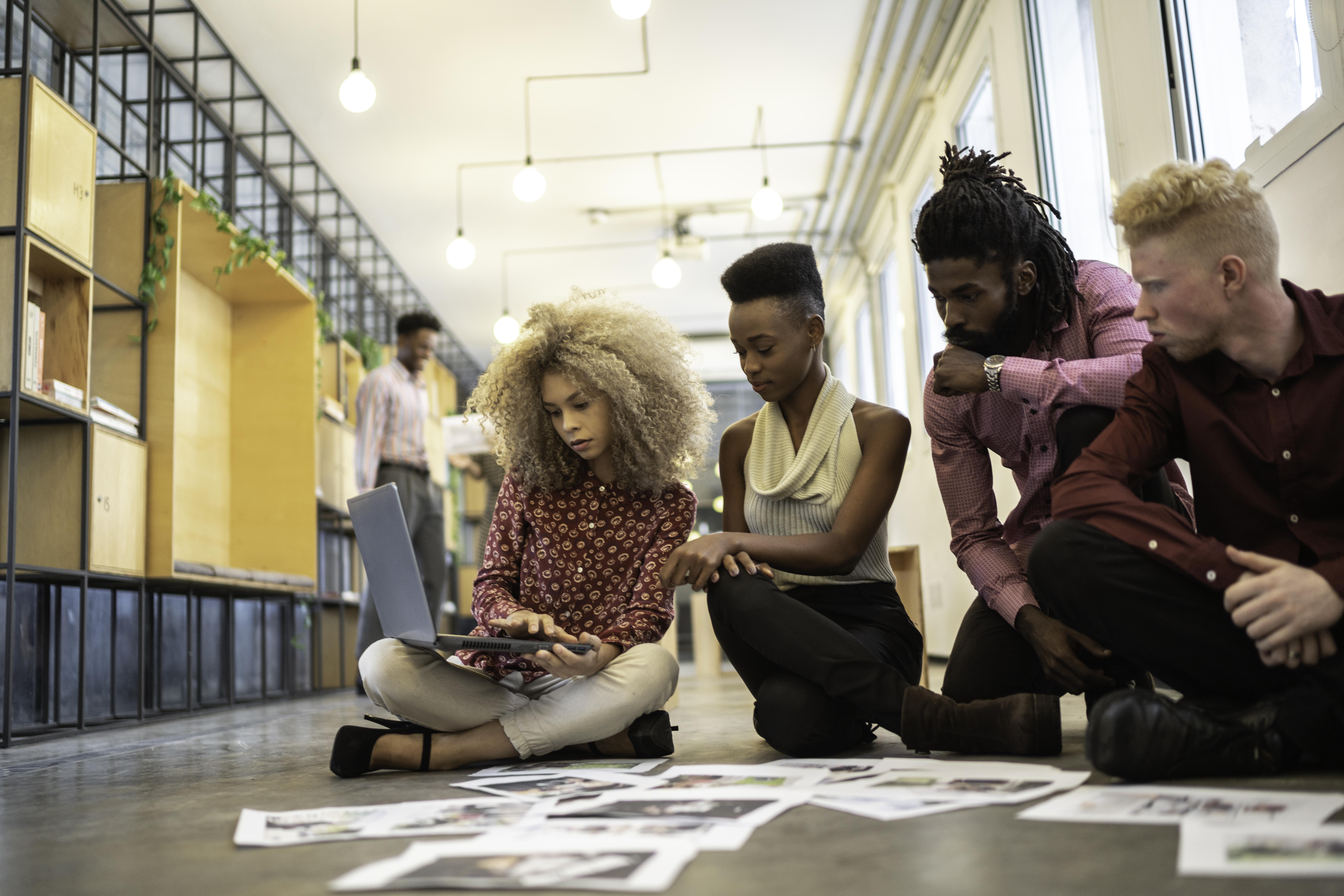 A group of colleagues sit on the floor while brainstorming a project.