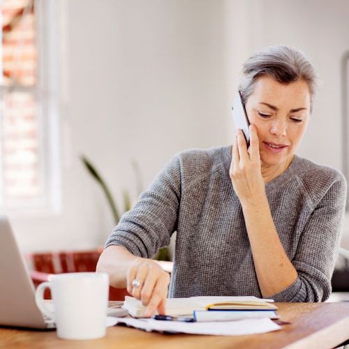 Professional multitasks by phone and notebook while managing tasks, reflecting AI-assisted request triage.