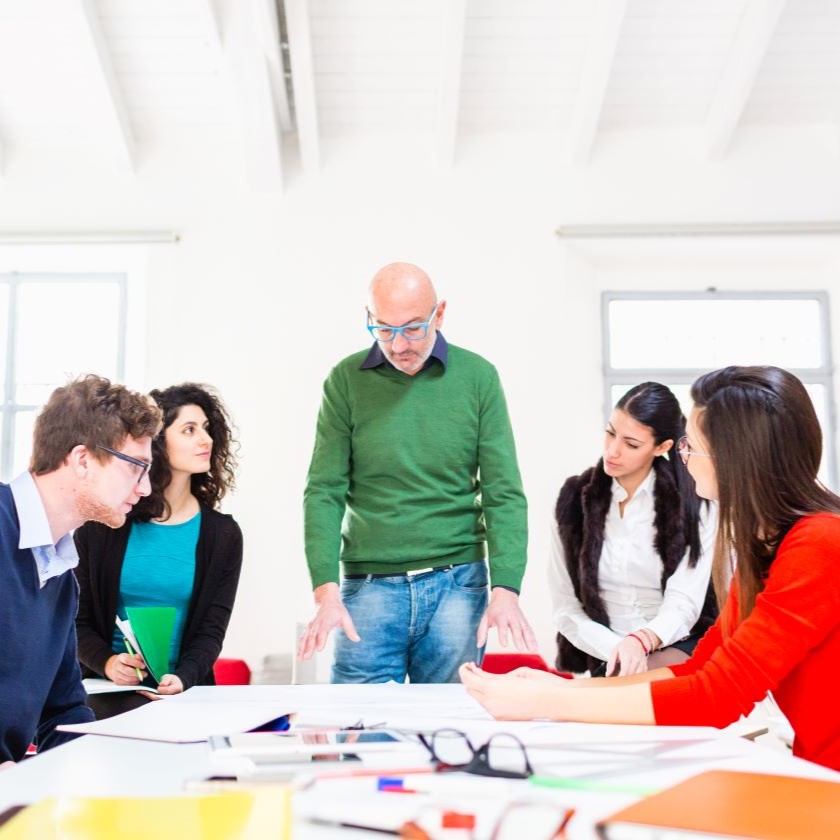 Colleagues collaborating on marketing strategy around table, focused on written campaign materials.