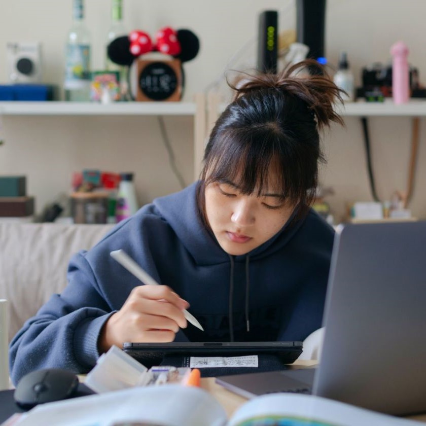 A focused individual searching through digital notes on a tablet, workspace filled with papers and devices.