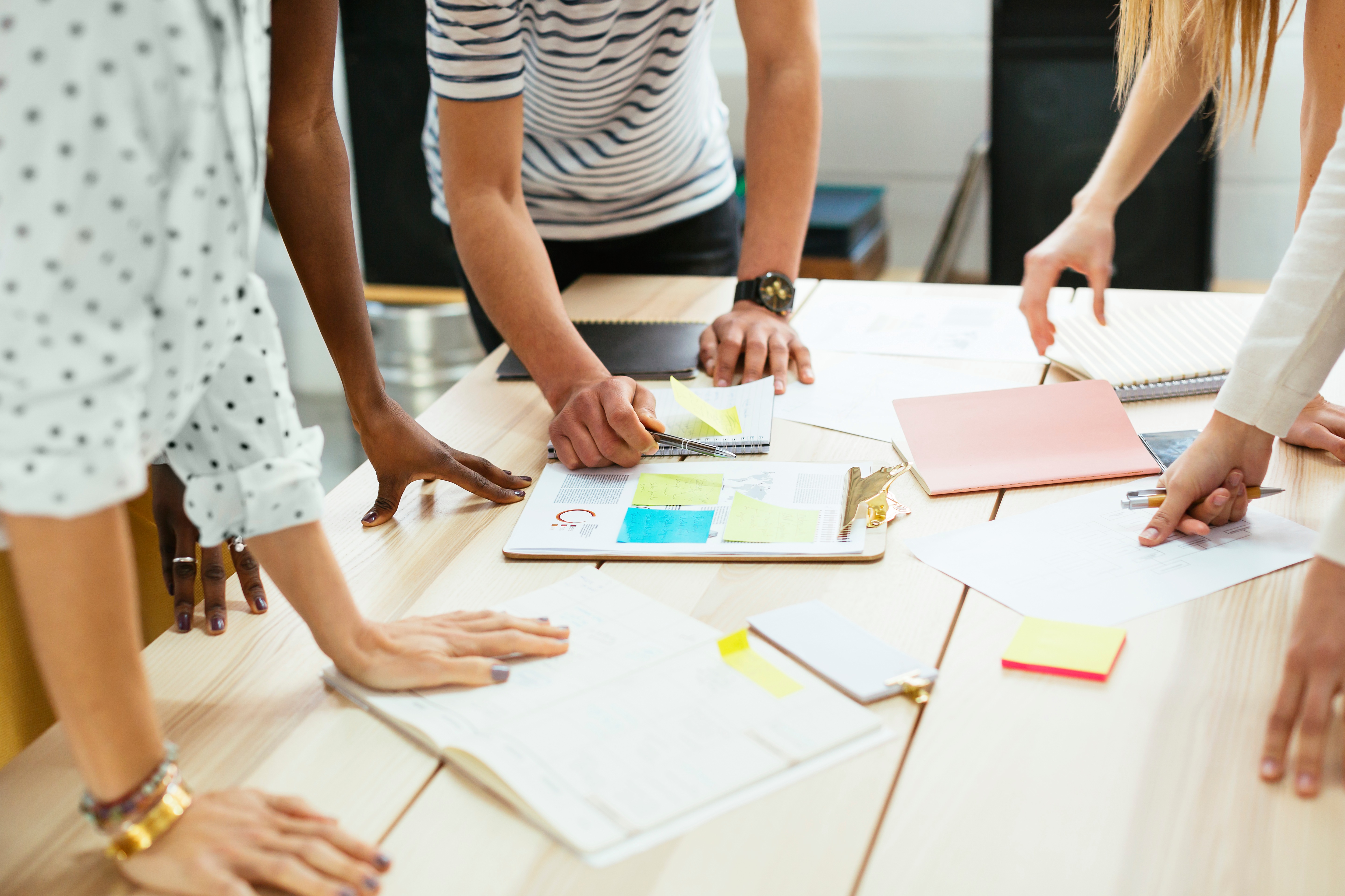 People stand around a desk with papers and notebooks while discussing an idea.