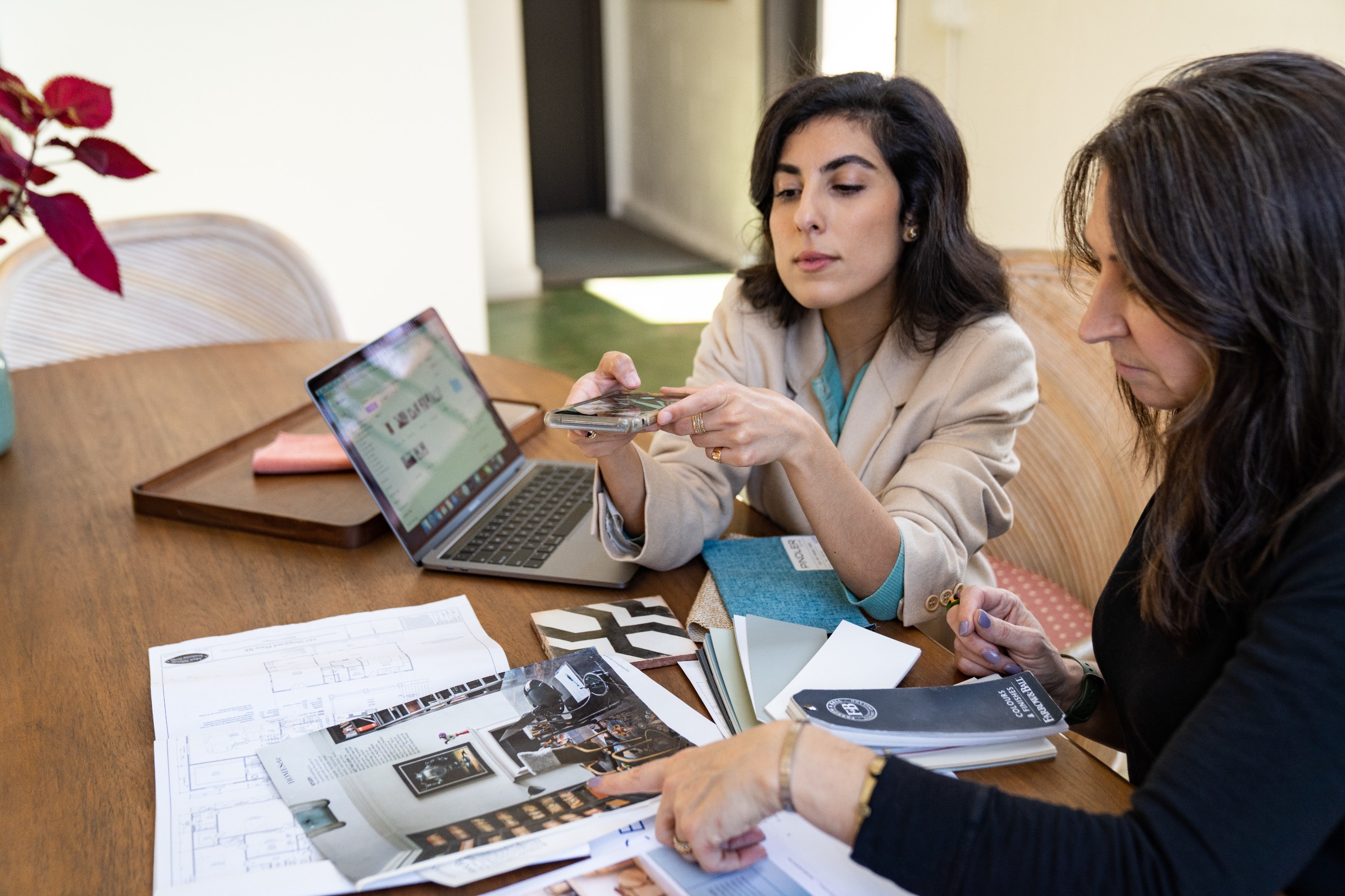 Two professional people reviewing printed materials and color swatches at a table with a laptop and smartphone.