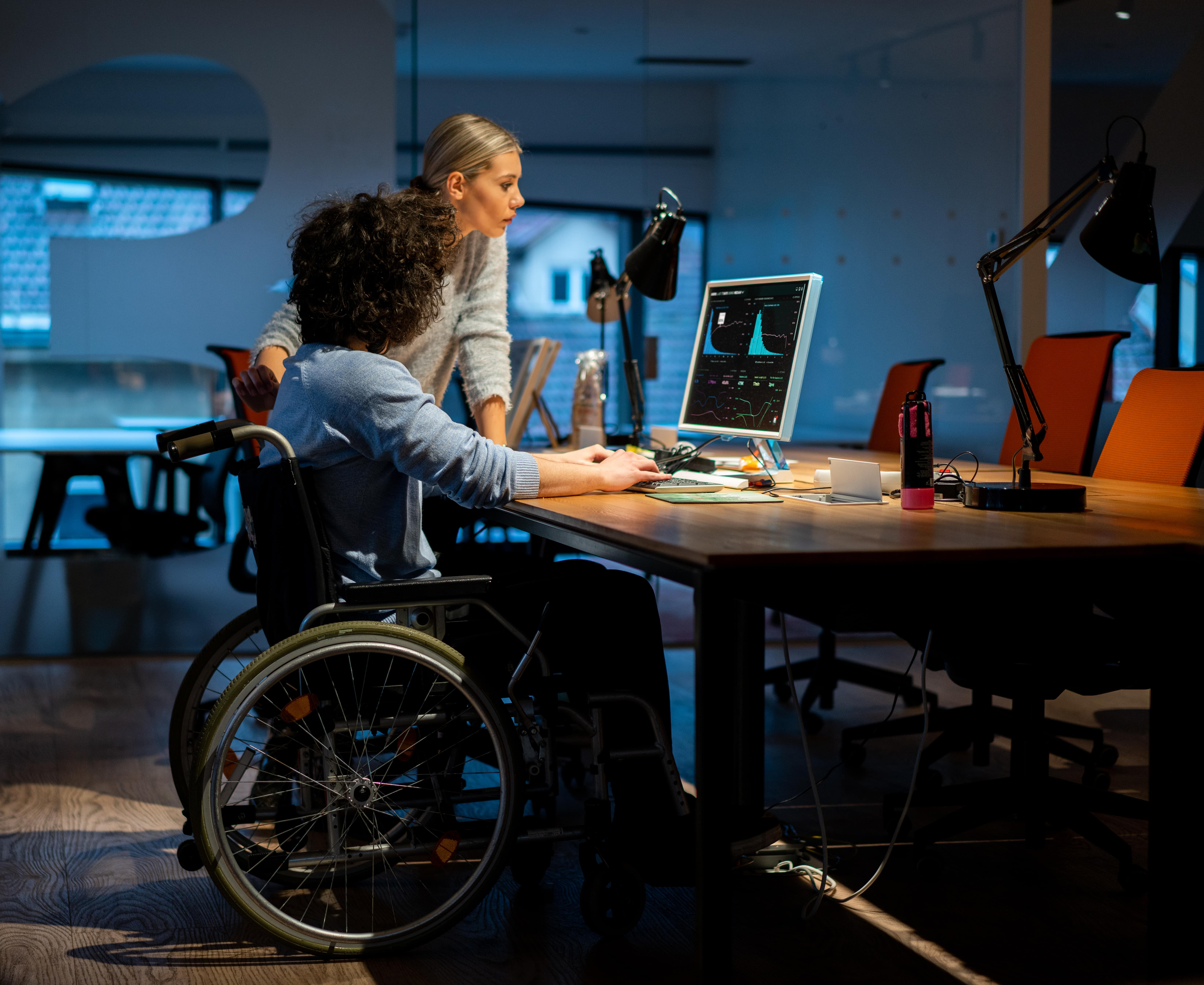 Two colleagues gather at a computer monitor while considering a task.