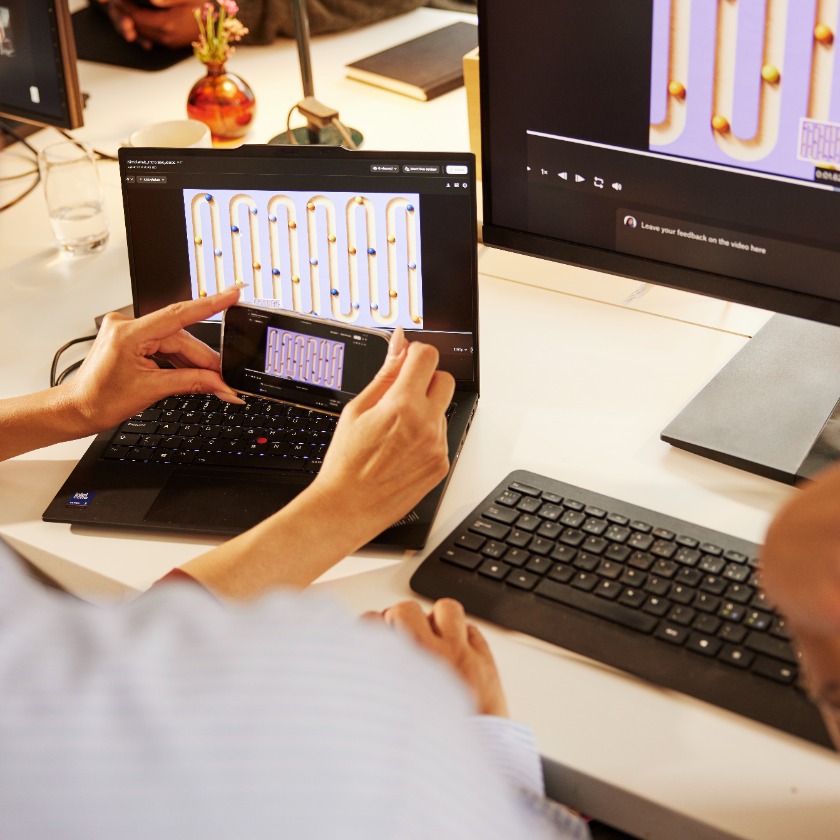 A person working on a project sits at their desk while looking at a video on multiple devices.
