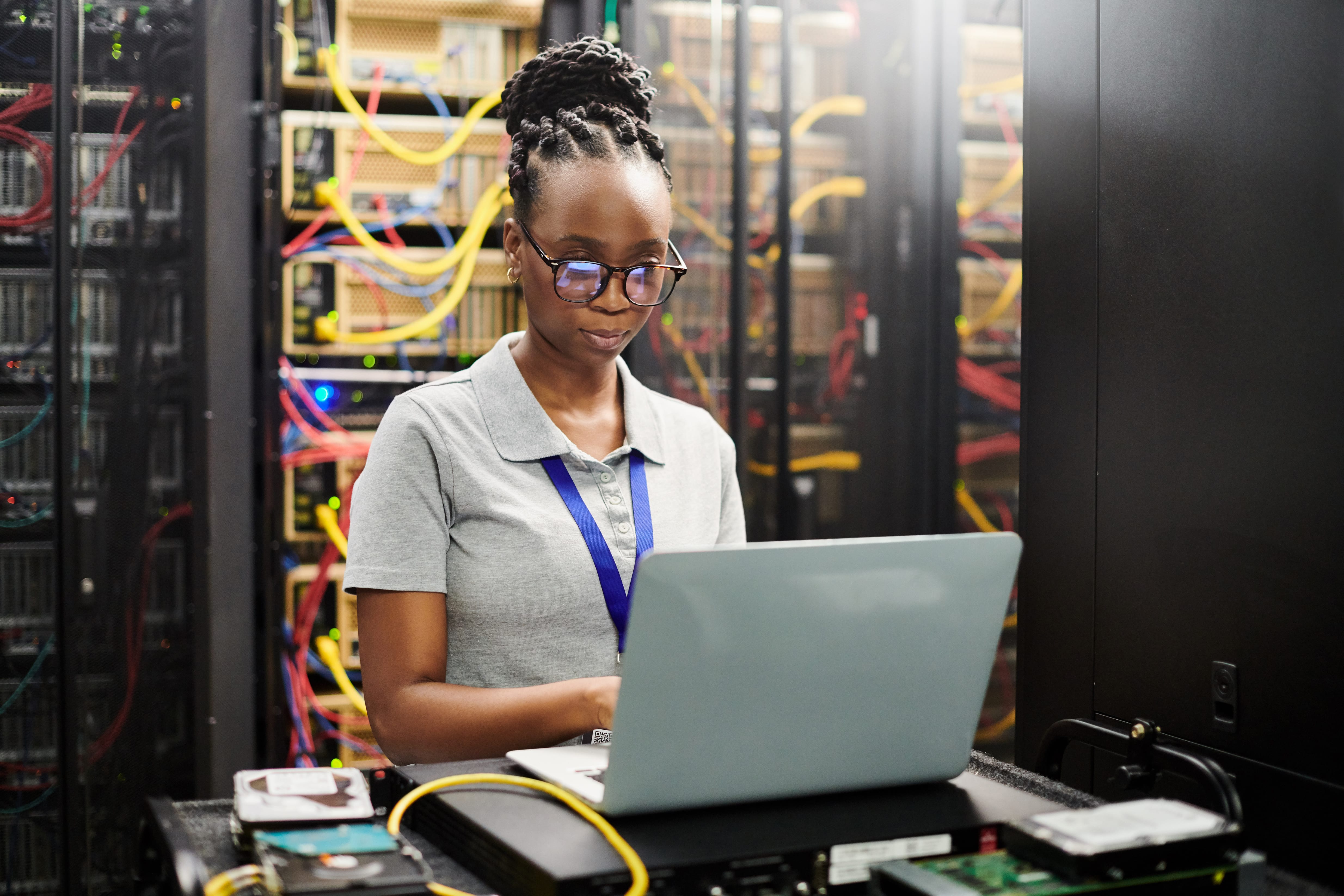 An engineer attends to a task on while working on a laptop in the middle of a large data center.