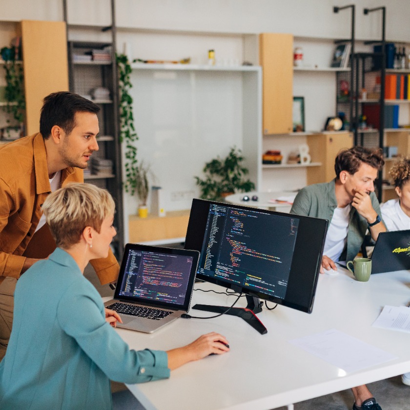 Busy design team collaborating across desks in a modern shared workspace with laptops and visual tools.