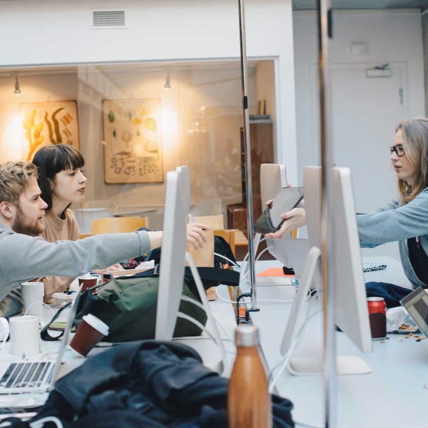Team members exchanging ideas and reviewing work on monitors and tablets during a collaborative work session.