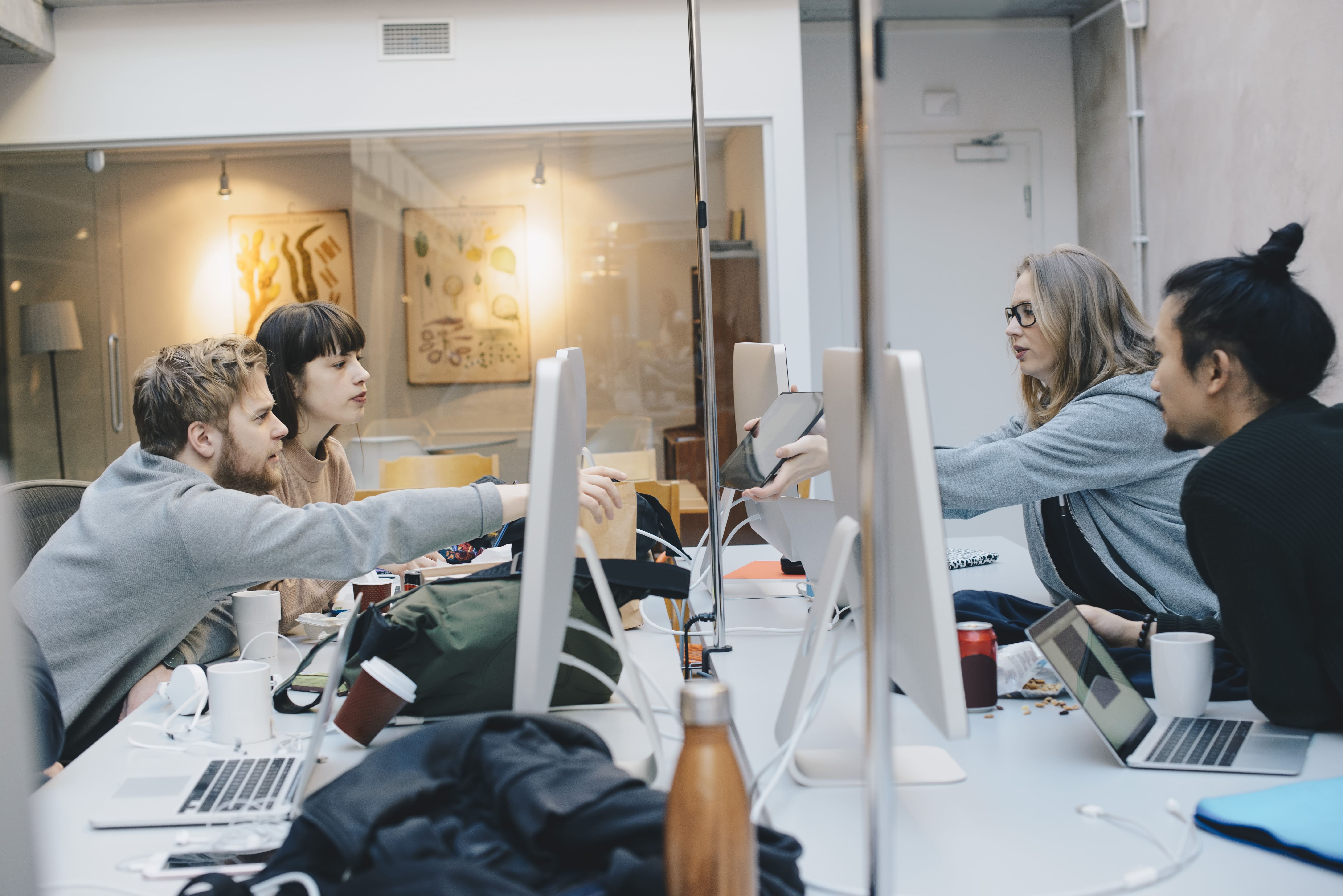 Group of coworkers collaborating at a long desk, working on desktop computers and sharing devices in a modern office.