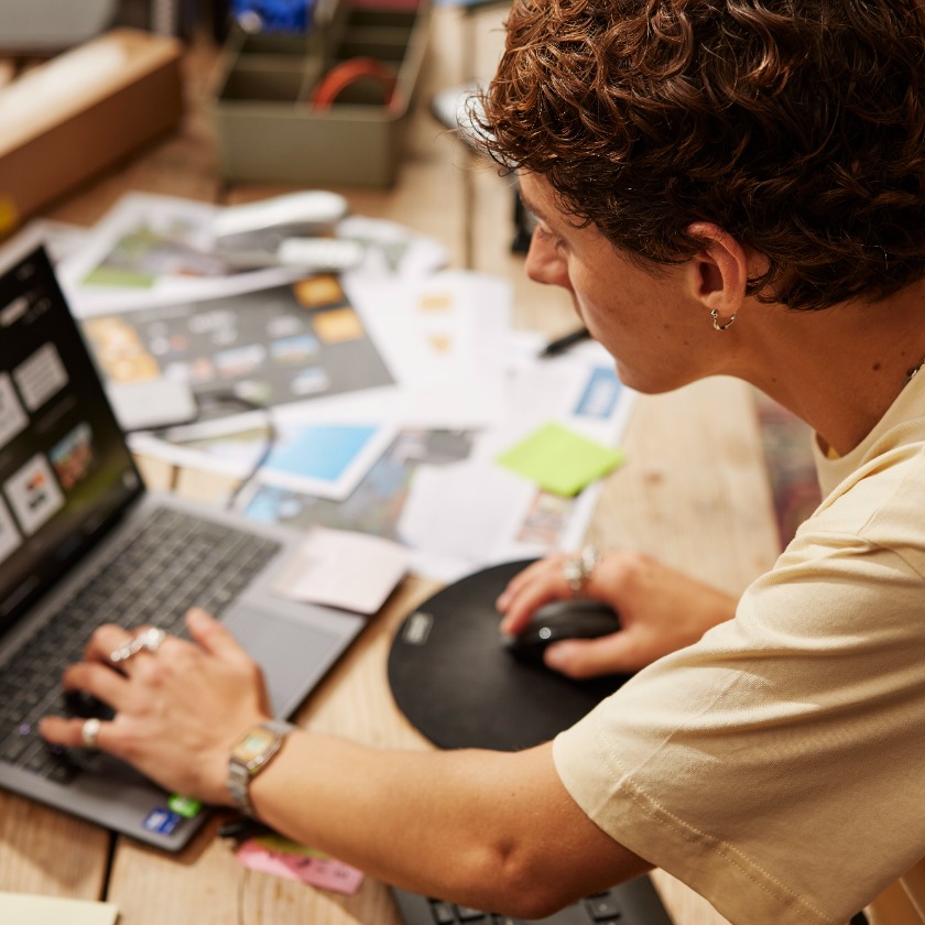 A person sits at their home desk while doing a task on their laptop.