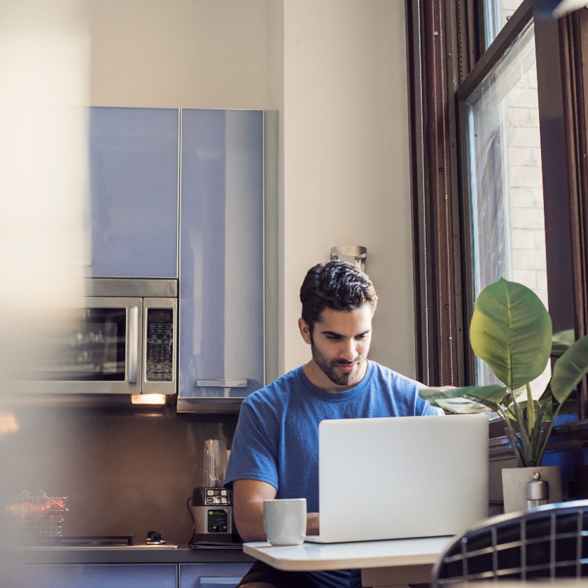 A person working on a laptop in a bright kitchen workspace, focused on the screen.