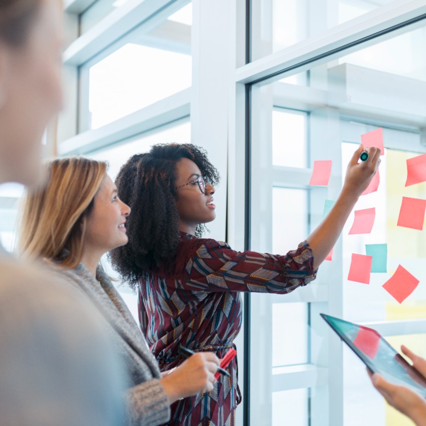 A group of people brainstorm together using sticky notes on an office window.