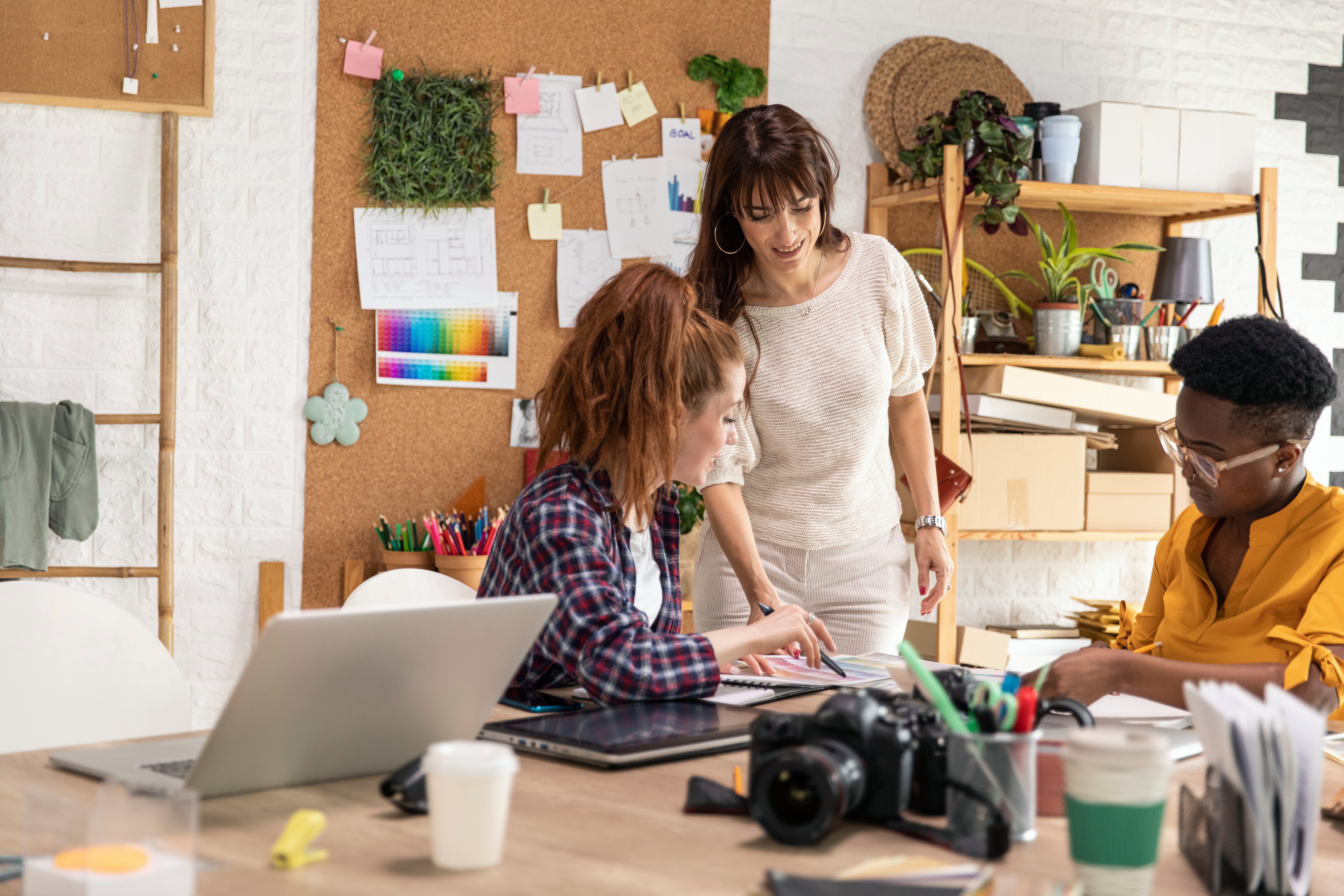 Creative team collaborating at a shared workspace, with a laptop, camera, tablet and printed documents on the table.