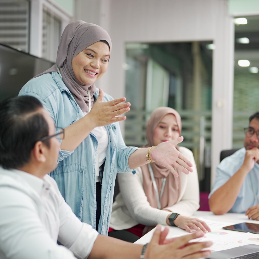 Four people gather around a meeting room table while discussing a project.