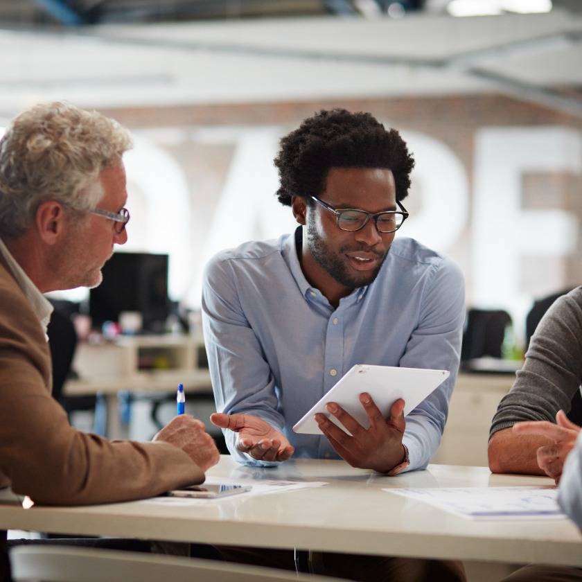 Group of colleagues at a table, discussing shared information displayed on a tablet.