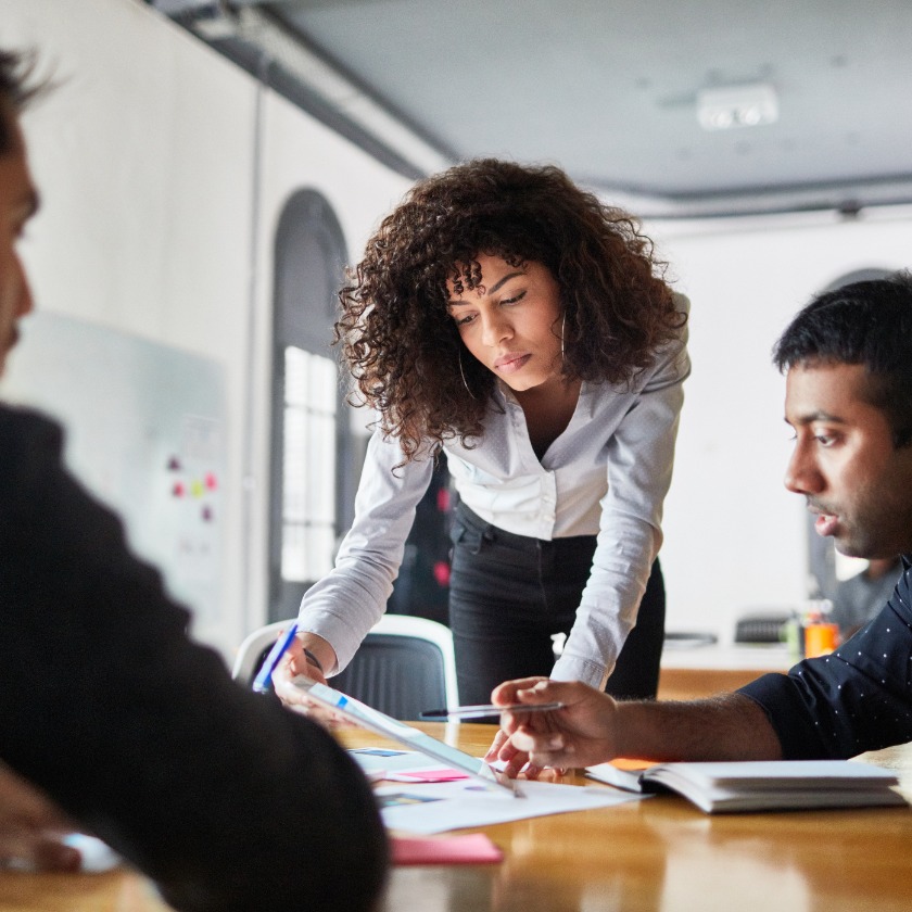 A person leans over a desk while looking at notes with a colleague.
