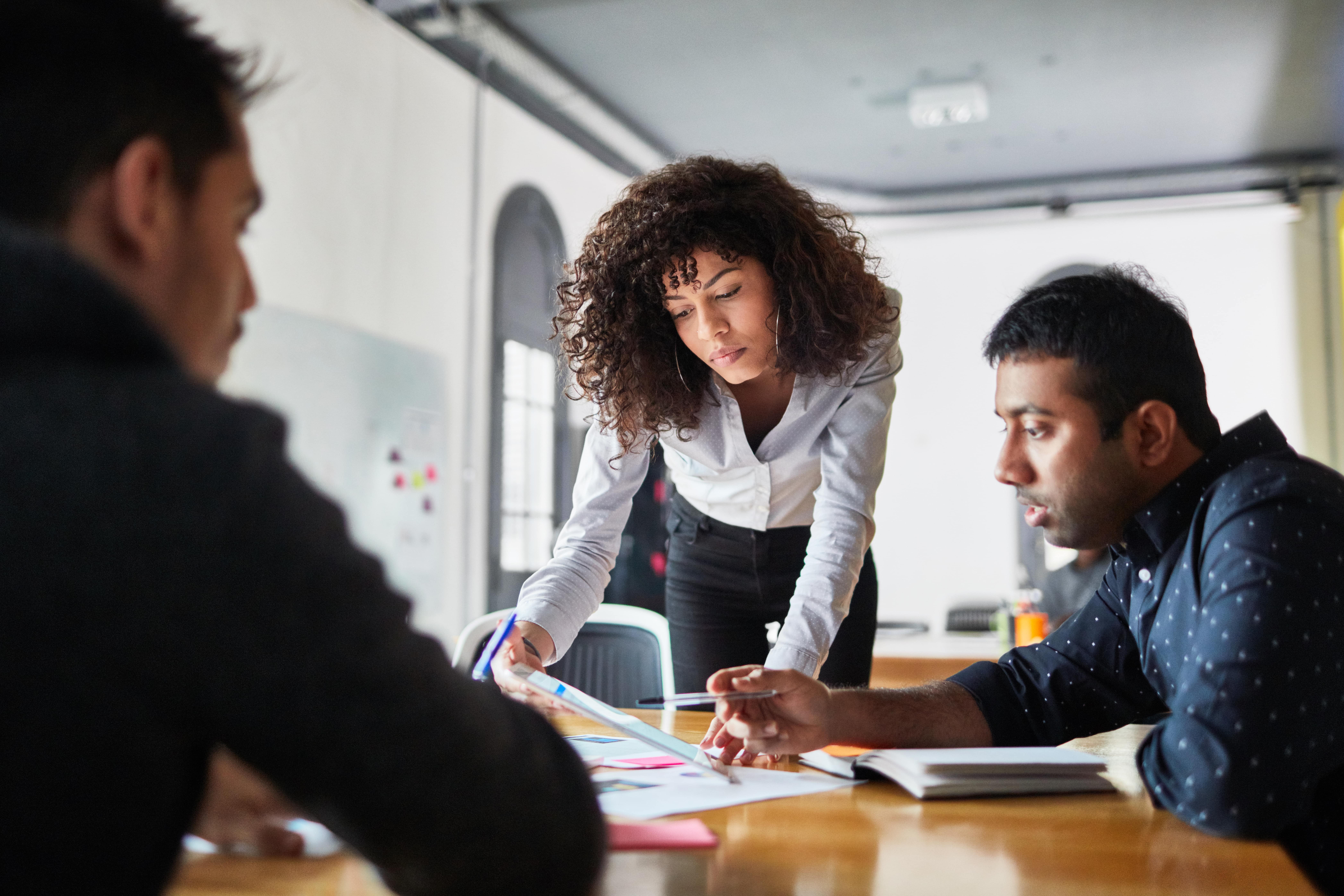 A person leans over a desk while looking at notes with a colleague.