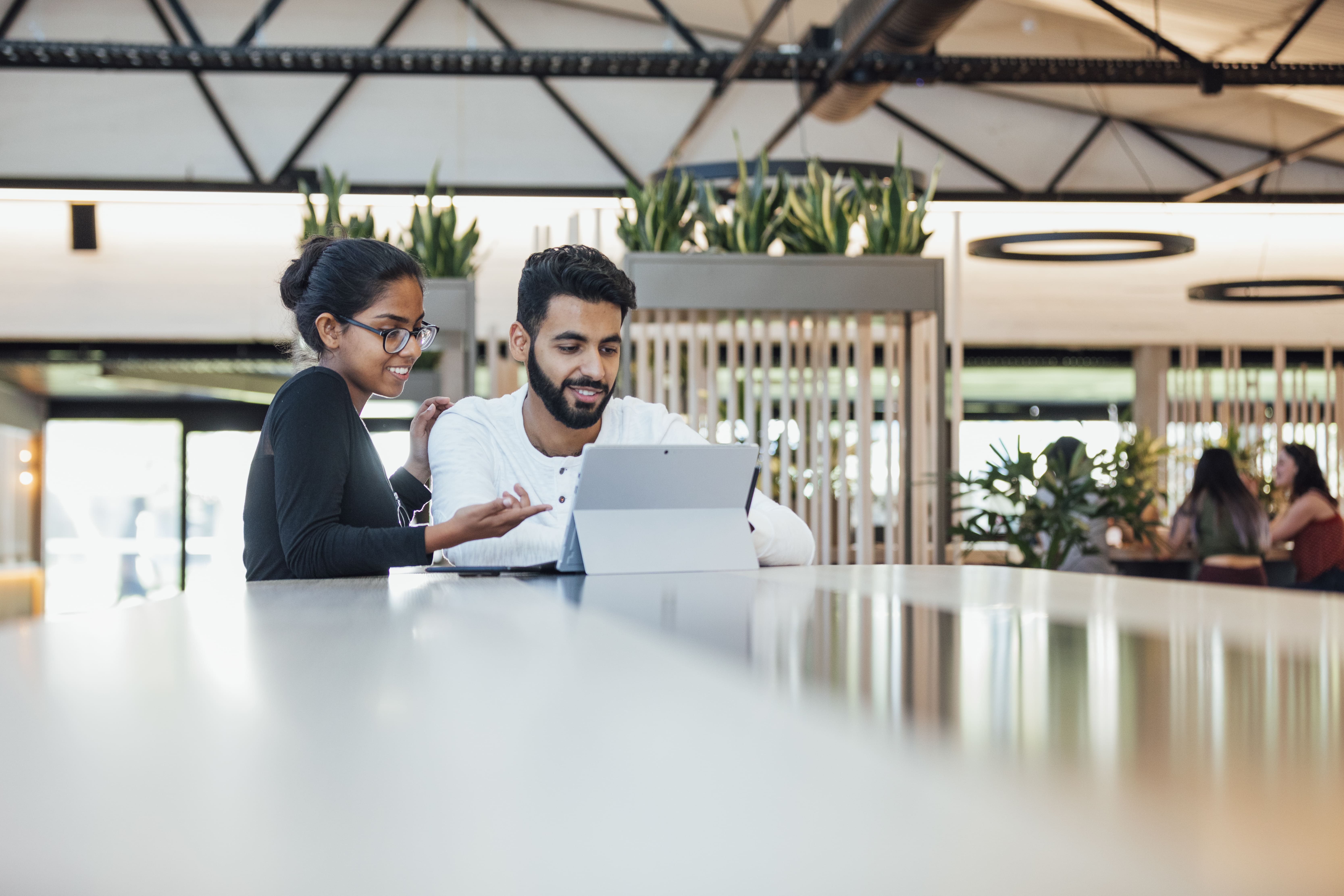 Two people reviewing a document together on a tablet in a modern office setting.
