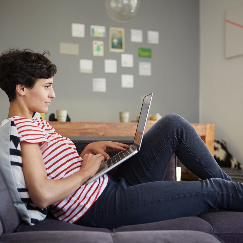 A person sits casually on their sofa while working on a laptop.