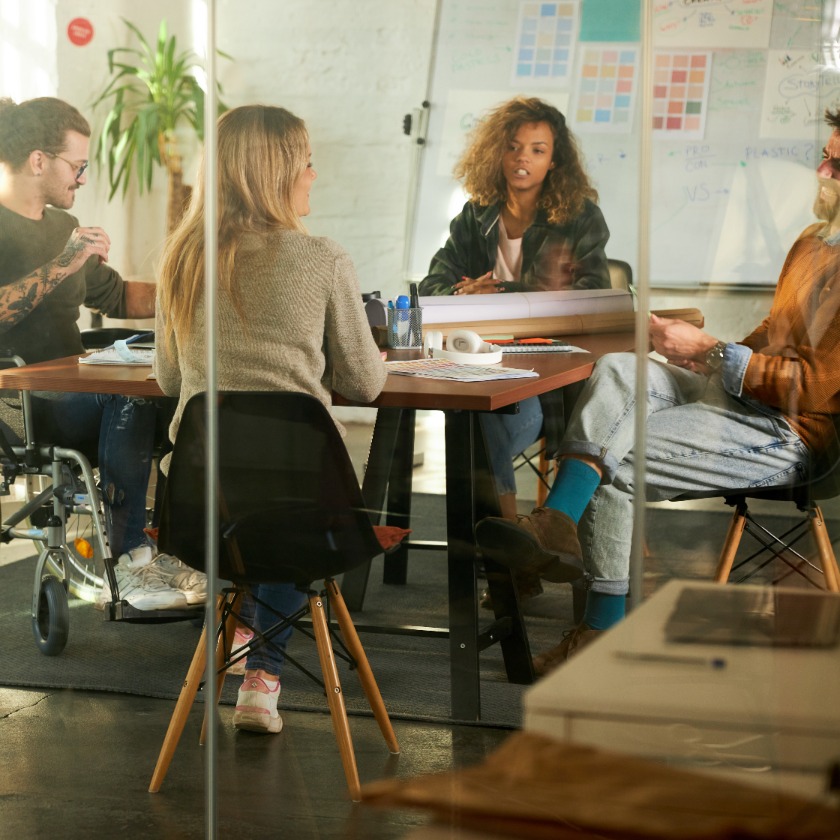 A group of colleagues discuss a project in an open plan meeting space.