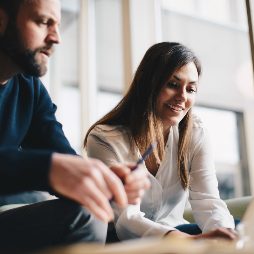 Two people sit at a desk in a breakout area having a discussion.