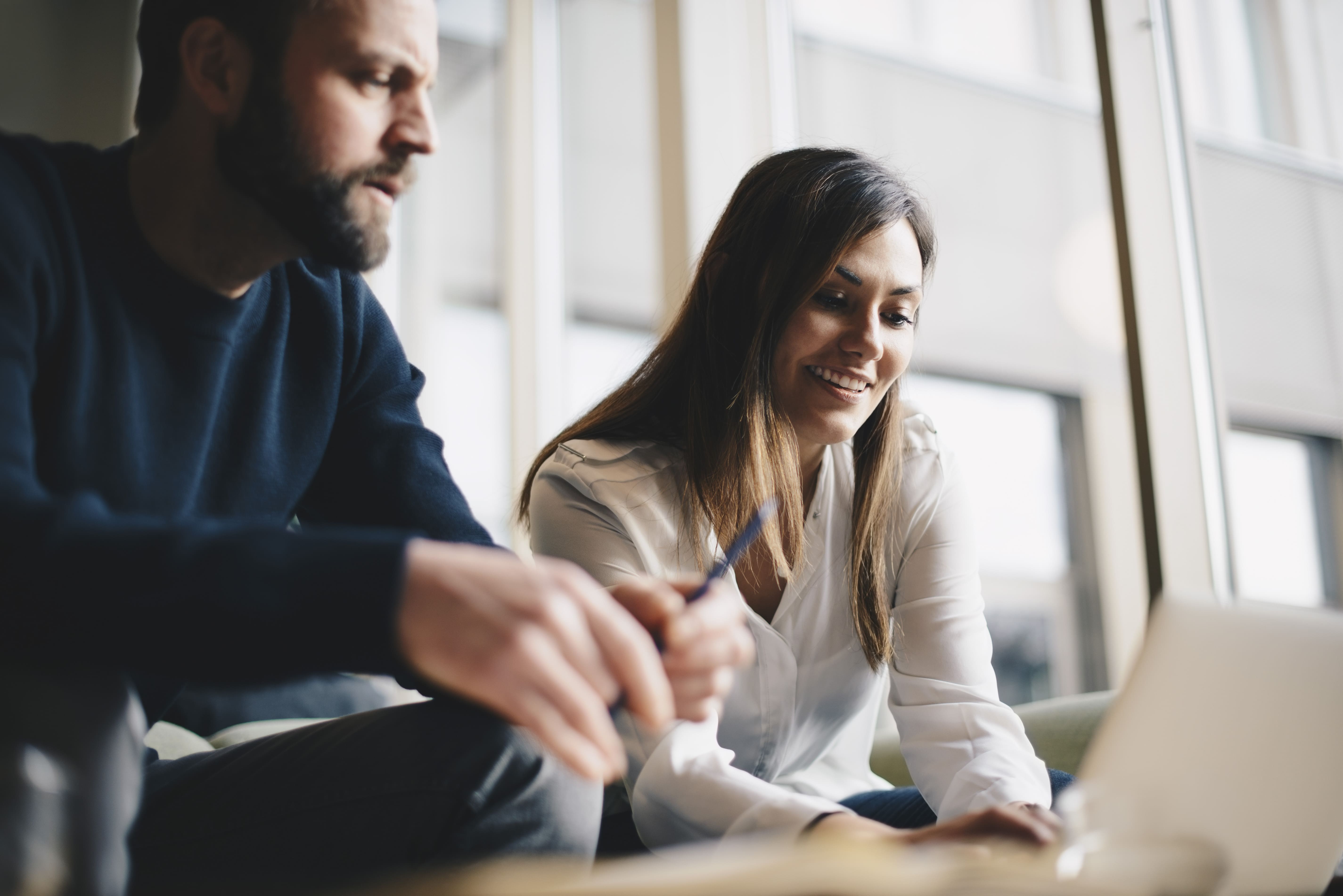 Two people sit at a desk in a breakout area having a discussion.