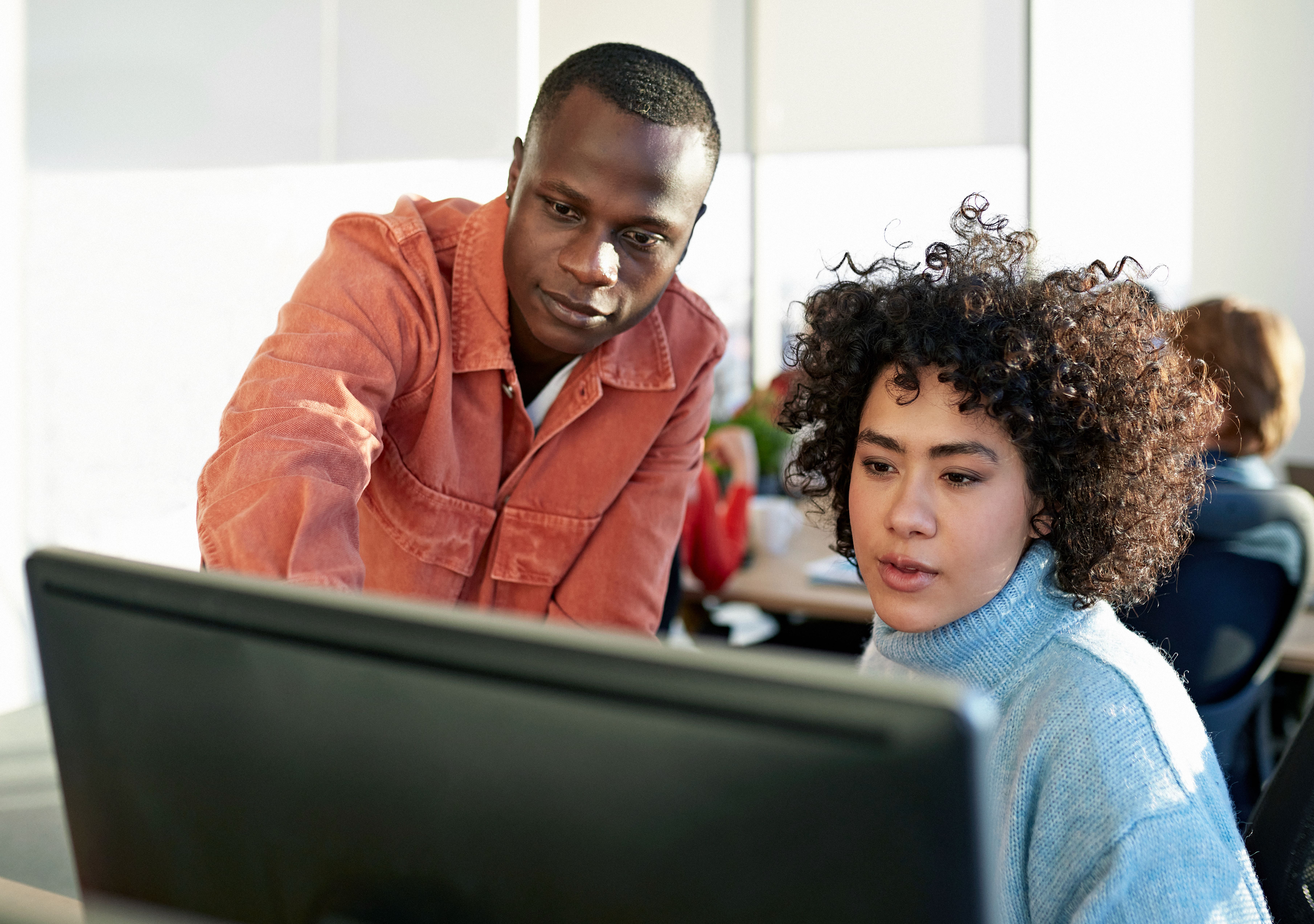 Two people at a desk with a computer and one person showing the other how to do a task.