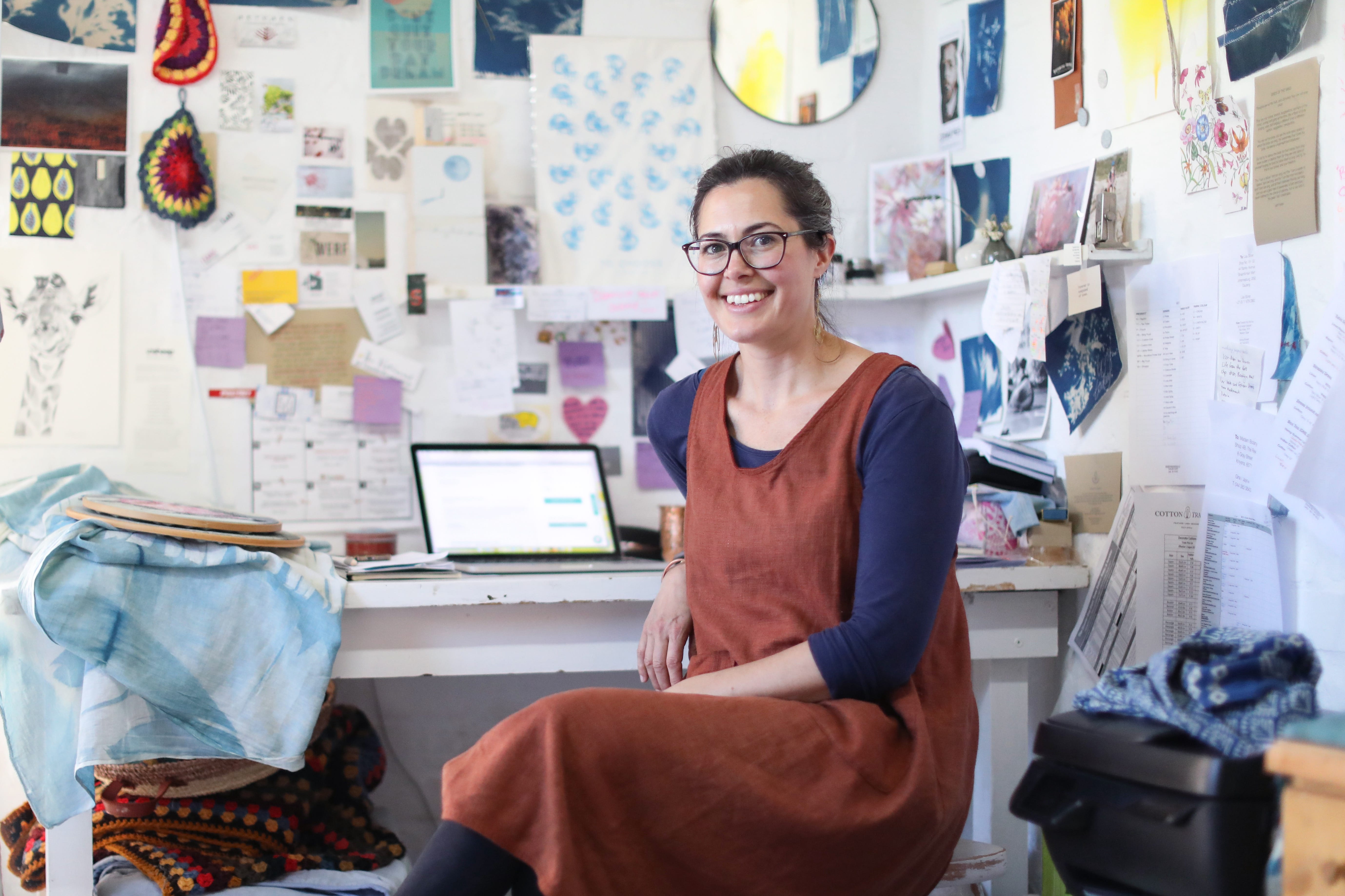 A person smiles at the camera while looking back from their desk in an art studio.