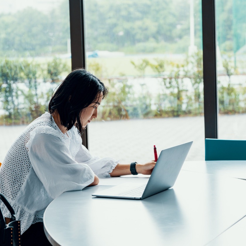 A person sits in a breakout area while making notes on their laptop.