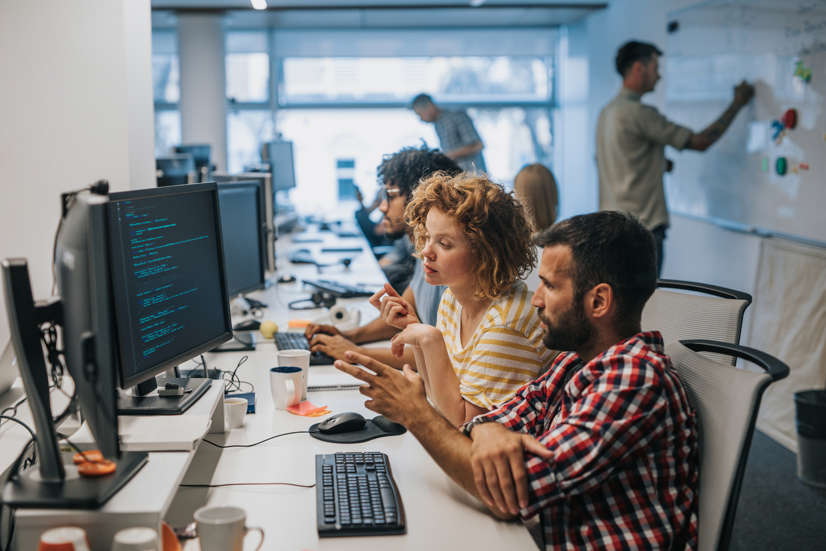 Team collaborating at computers in a modern office, discussing code and project details.
