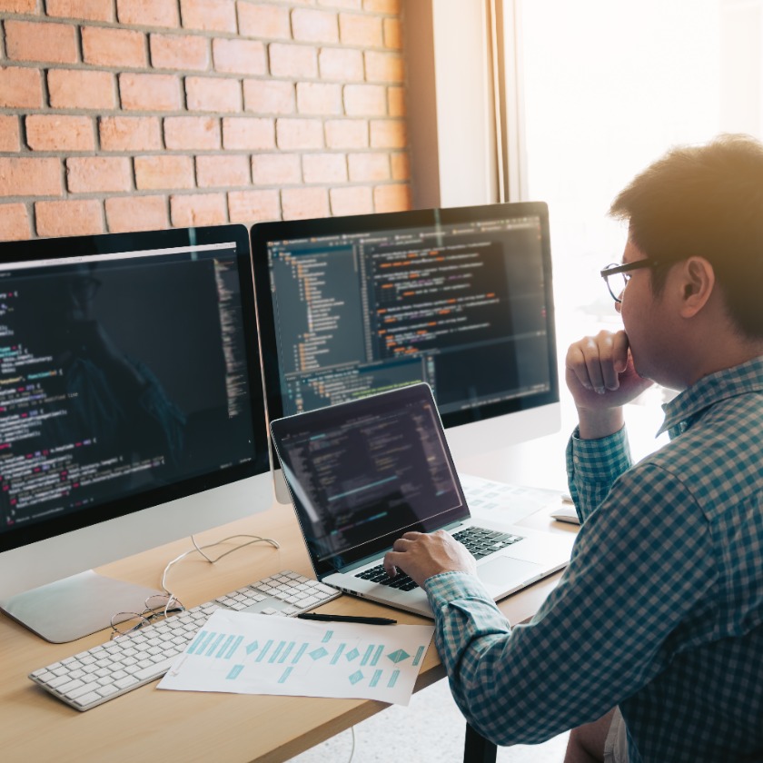 Developer working at desk with multiple monitors displaying code in a modern office