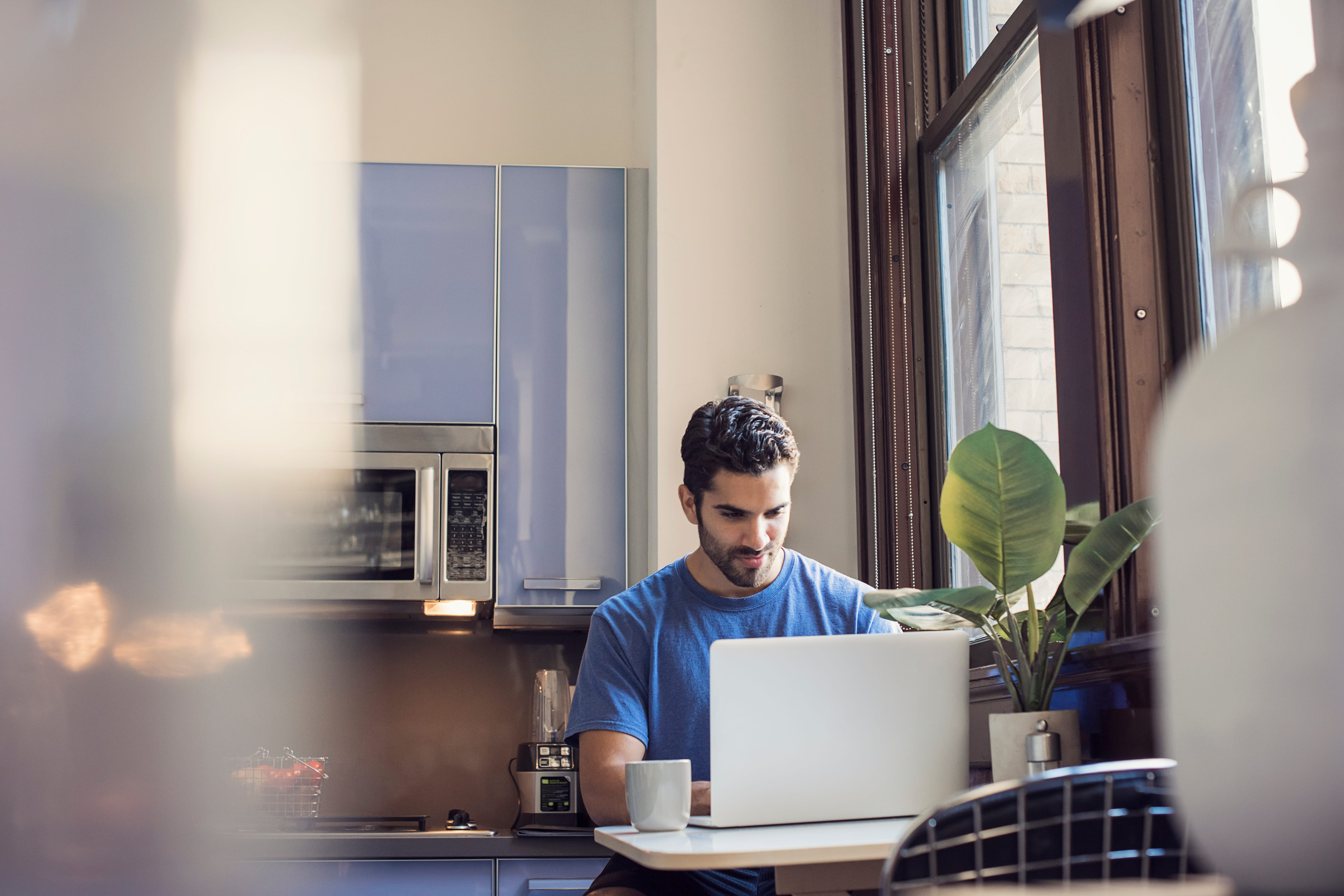 A person sits at their kitchen table while working on a laptop.