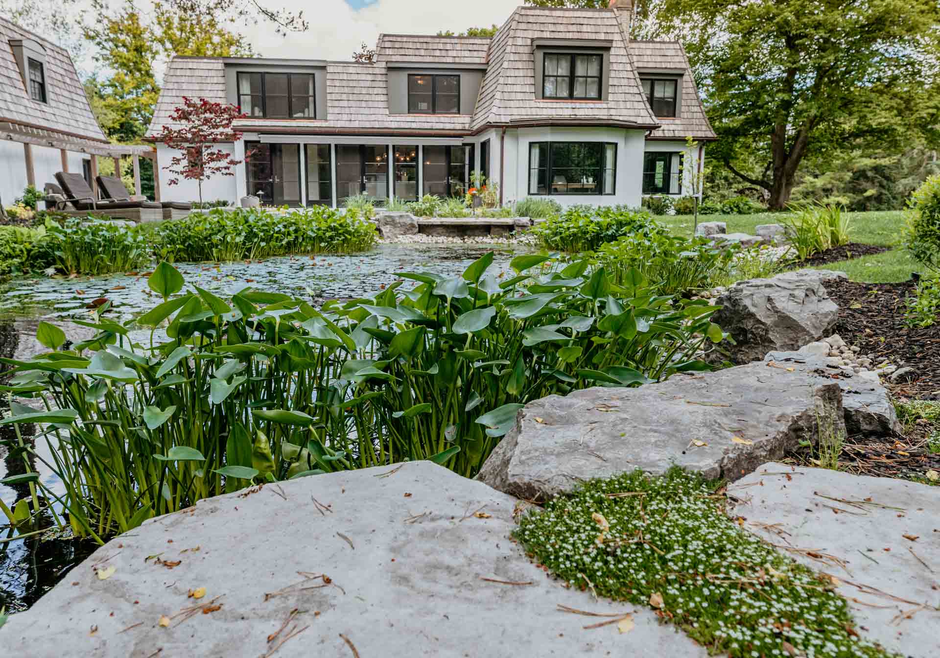 Custom designed landscape featuring a stone pond and water feature set within a private, lushly landscaped residential backyard.
