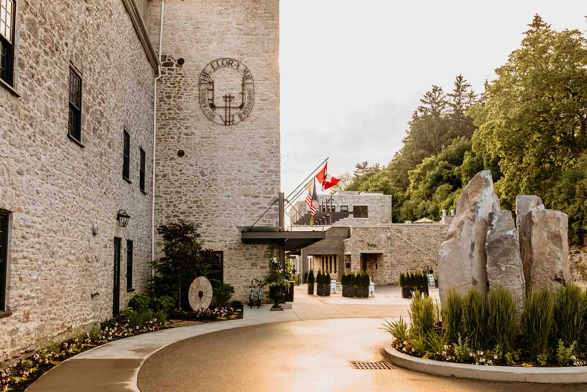 Elora Mill luxury landscape design and construction, masterly crafted entrance, featuring a natural stone sculpture, lush garden beds, retaining wall, and accents.
