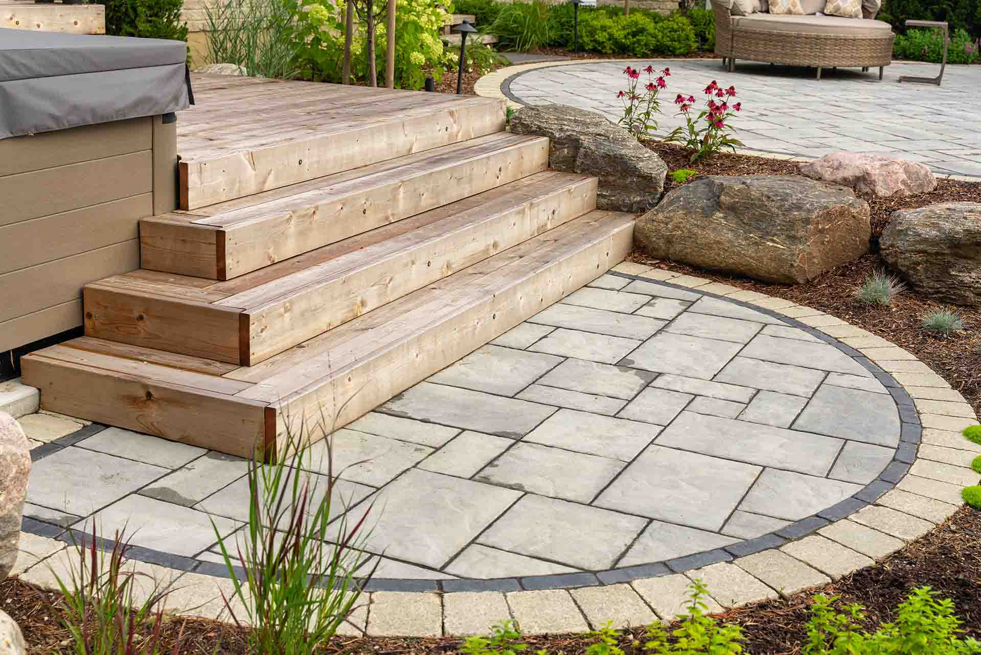 Custom deck and stairs surrounding a hot tub, with a natural stone pathway and lush, professional landscaping.