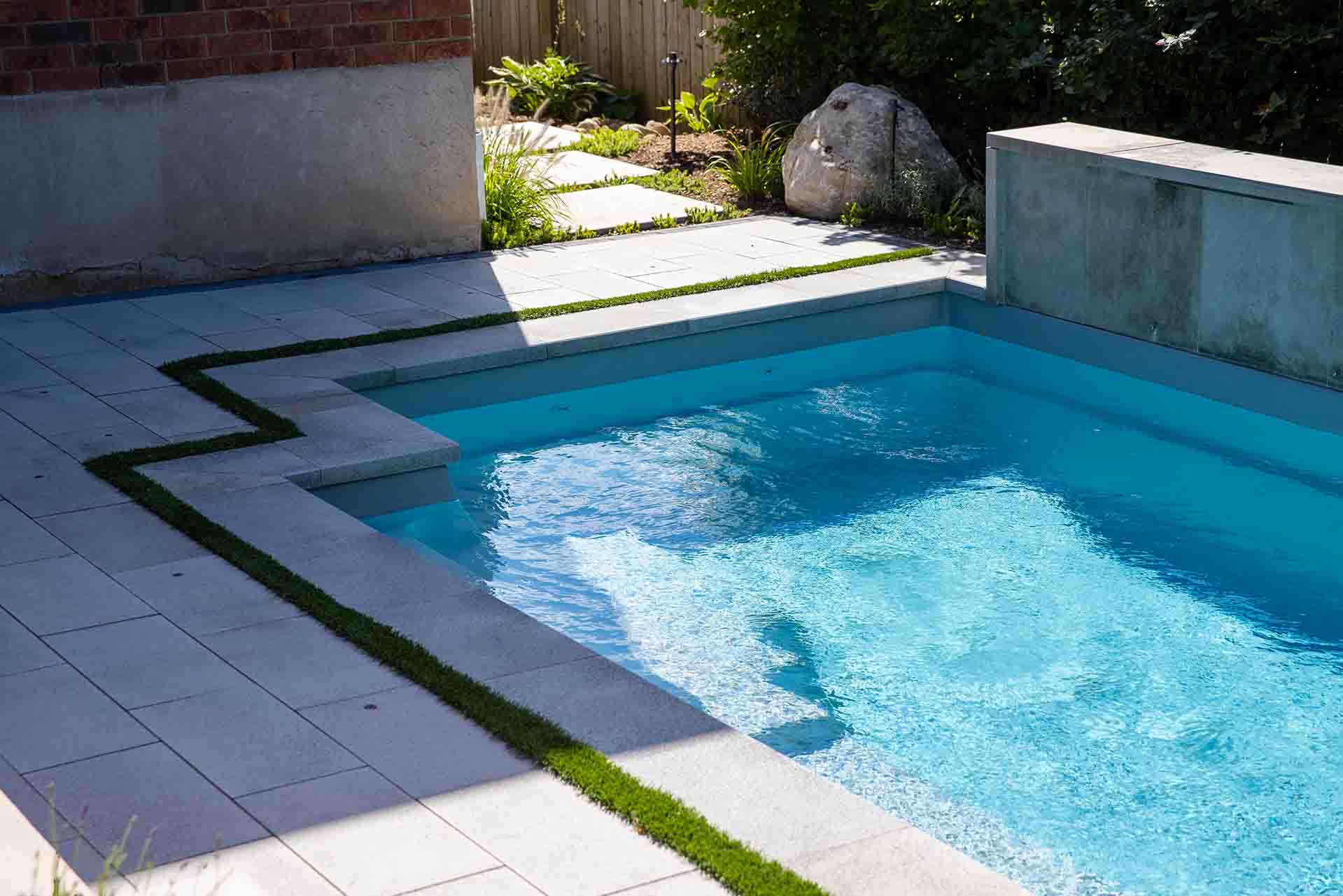 Inground pool with paver patio stone and lush garden beds.
