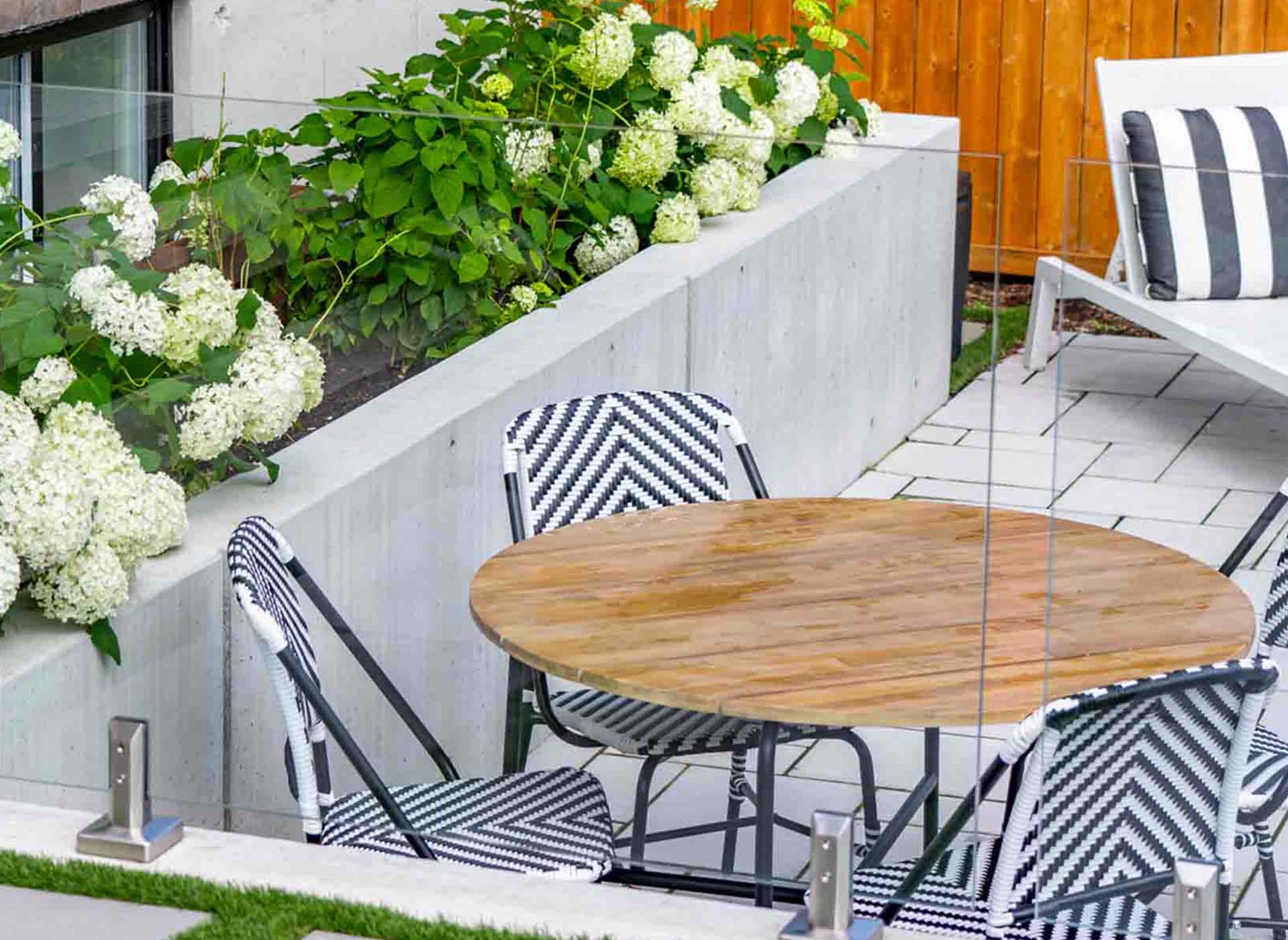 Modern outdoor sitting area surrounded by hydrangeas, glass railing, luxury pool, and timber pergola.