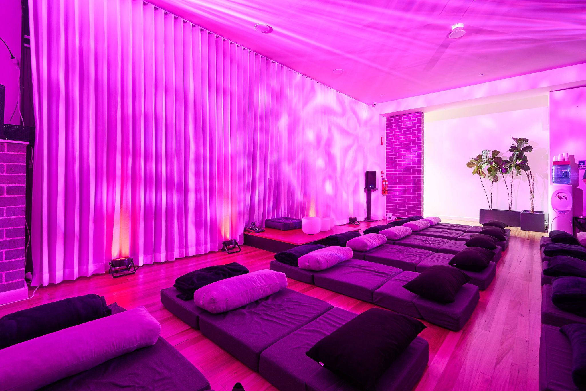 A breathwork studio with ambient lighting with yoga mats, bolsters and blankets laid out.