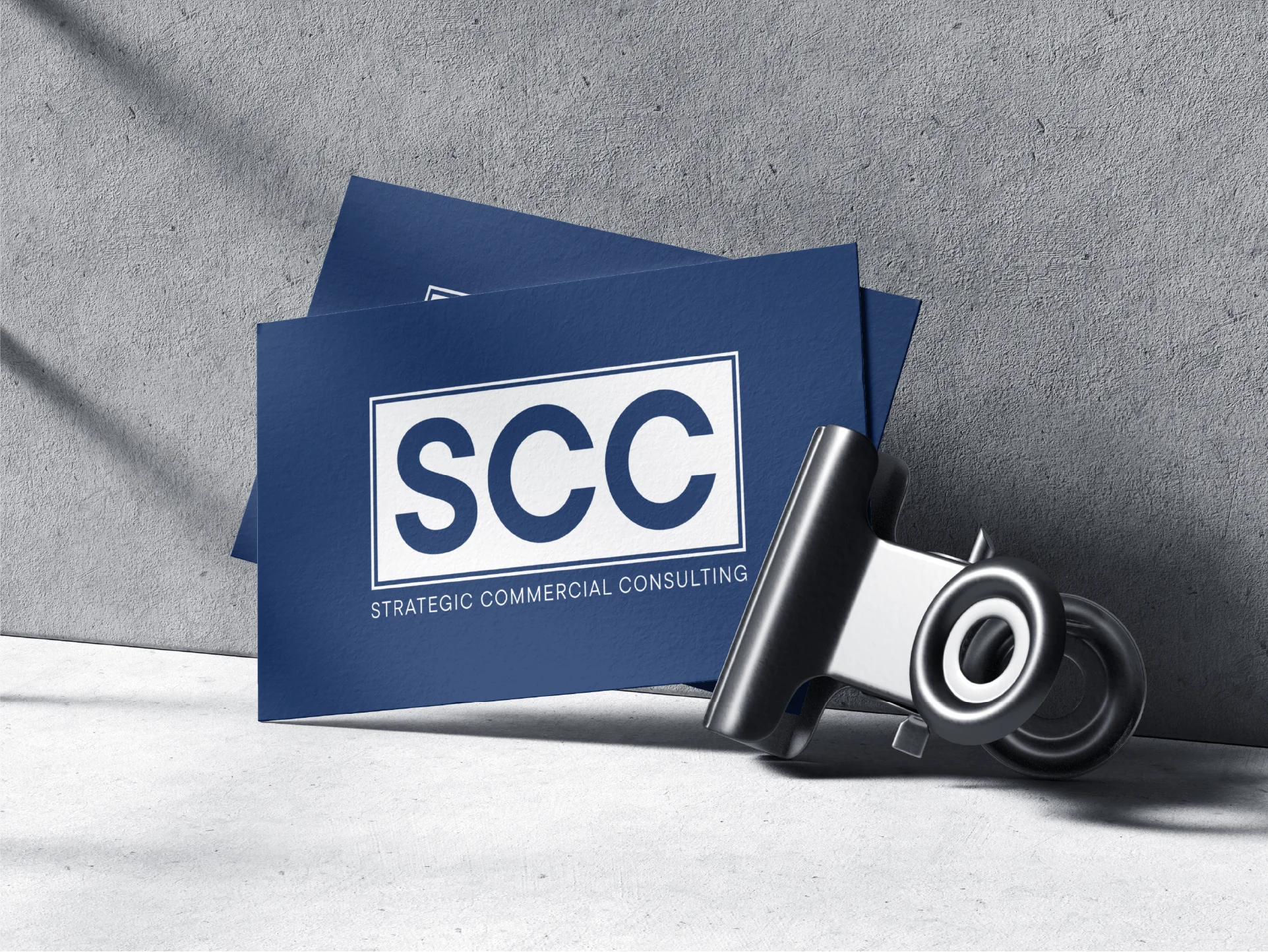 Blue business cards with white text 'SCC Strategic Commercial Consulting' clipped together on a gray surface.