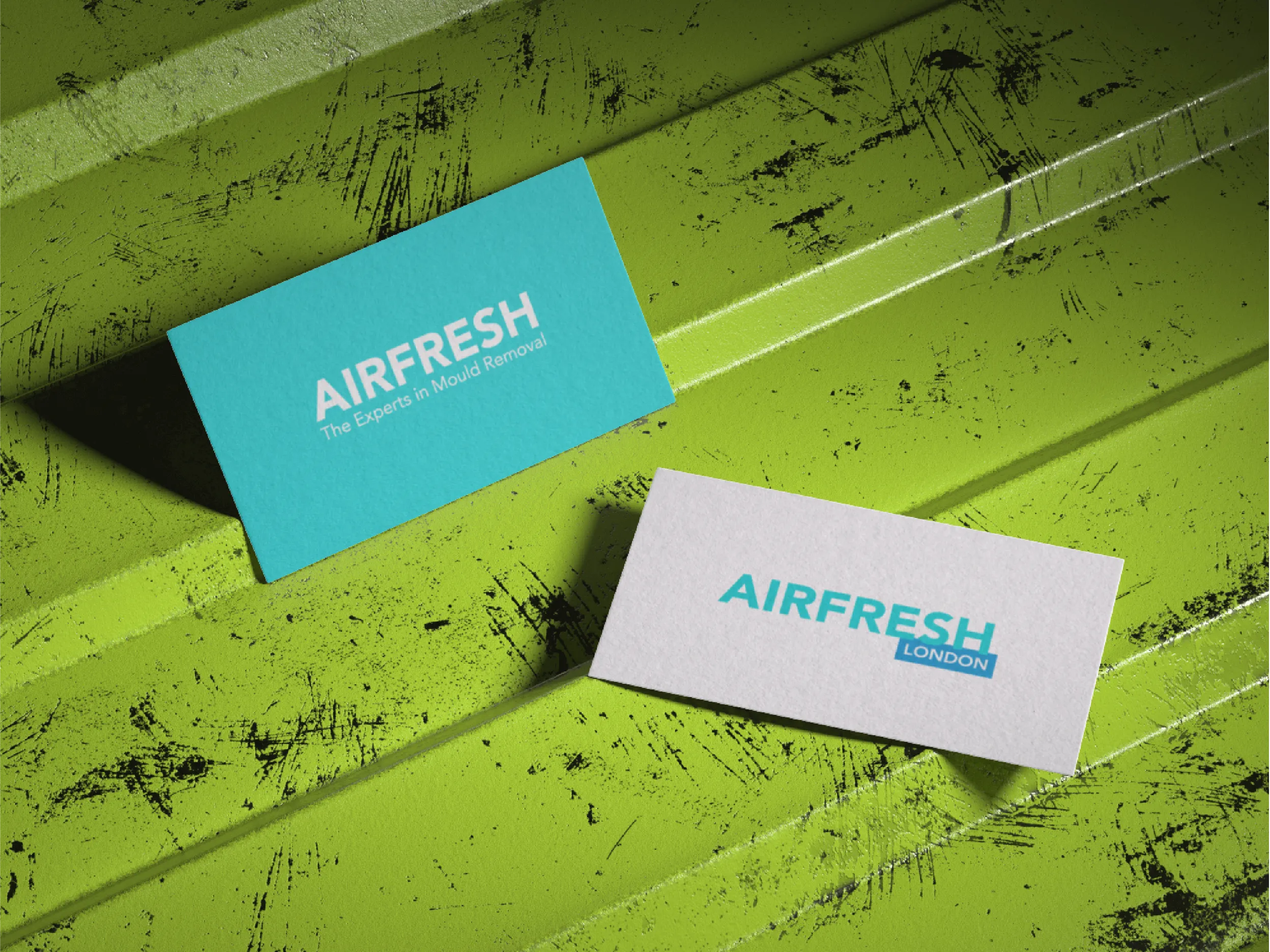Two Airfresh business cards on a scratched green metal surface, one turquoise with white text, the other white with turquoise text.