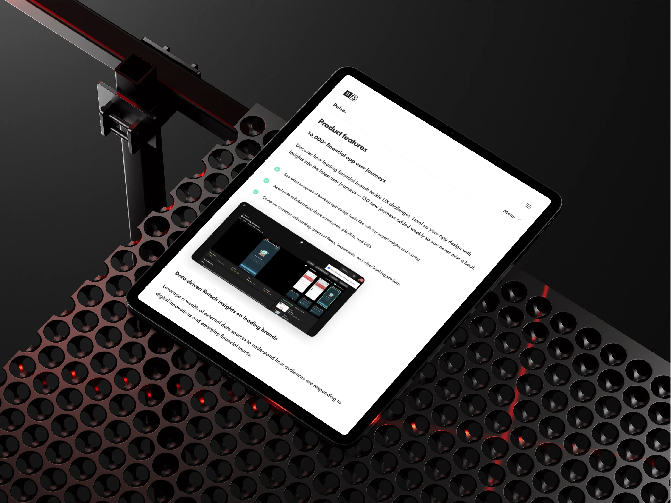 Tablet displaying a webpage with product features of a financial app, resting on a black perforated surface with red lighting underneath.
