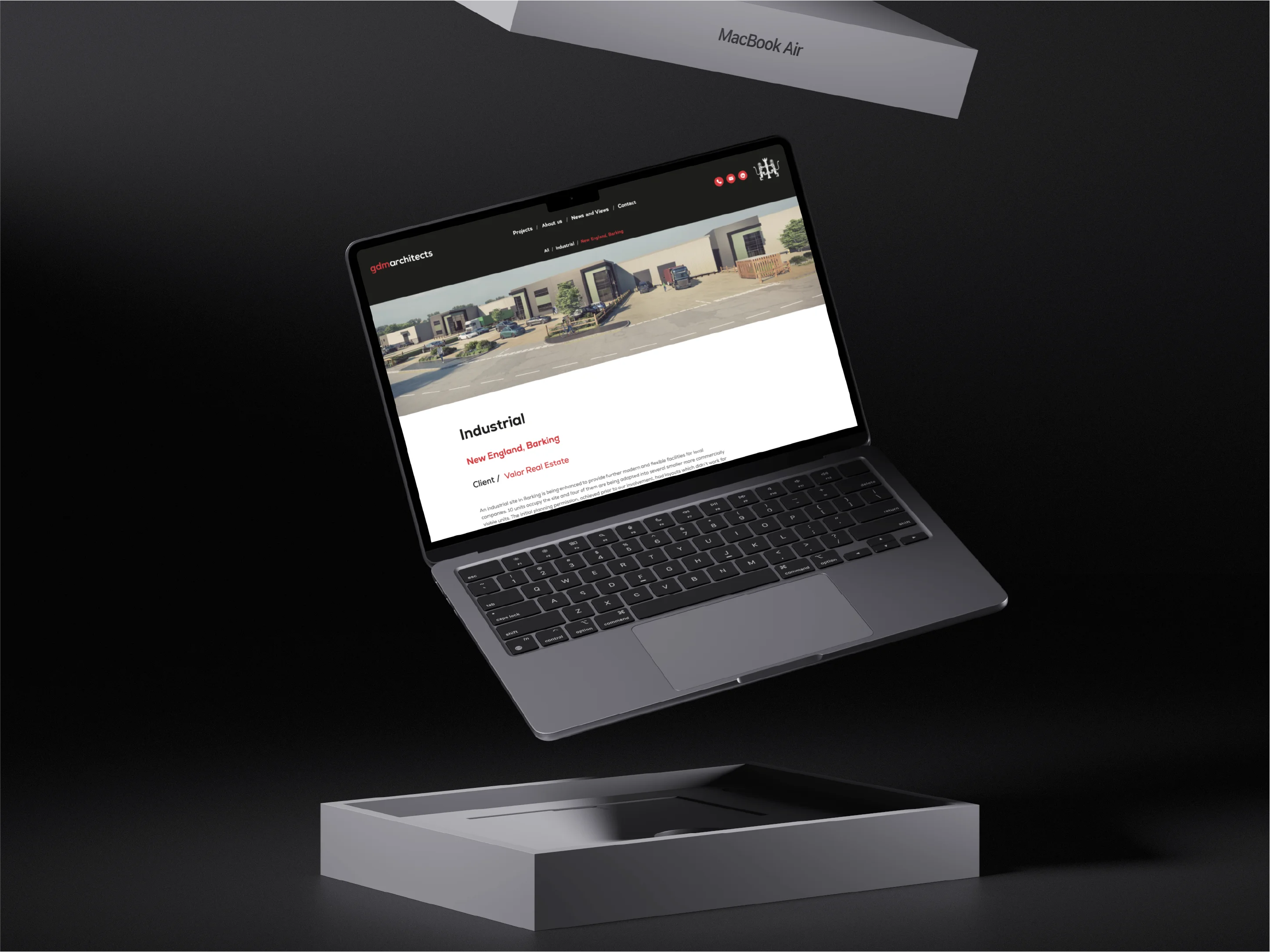 Open MacBook Air laptop floating above its empty box on a black surface, displaying a website for gdm architects featuring an industrial project.