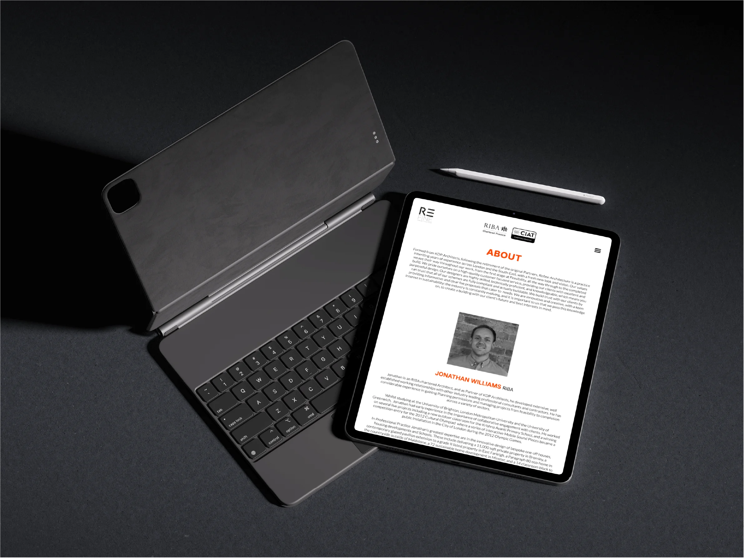 Tablet with keyboard case and stylus resting on a dark surface, displaying an about page featuring Jonathan Williams, RIBA.